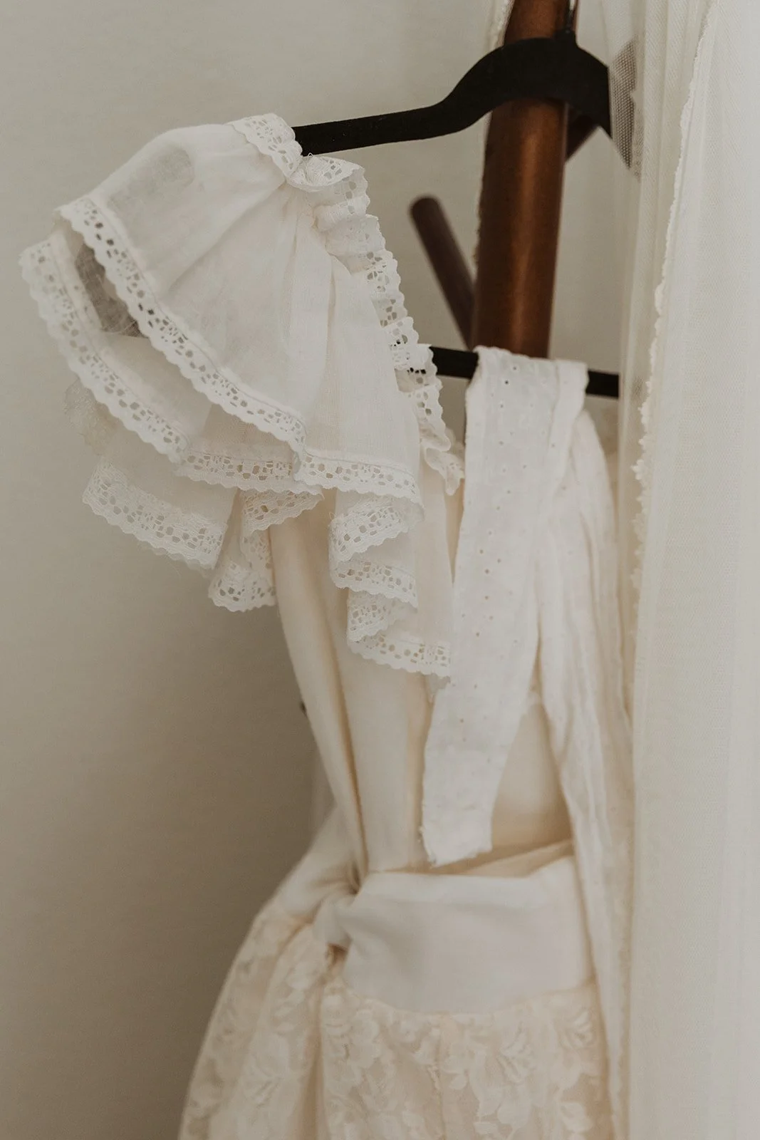 Close-up of lace wedding dress hanging on wooden rack showing textured detail