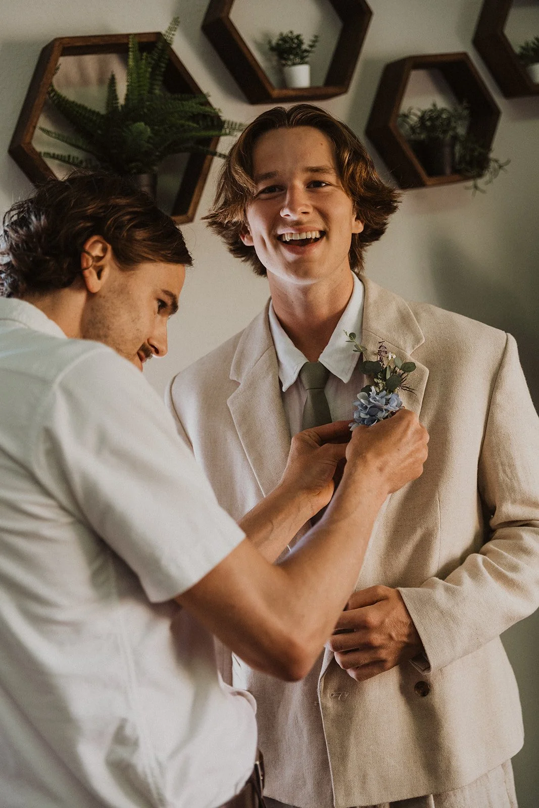 Groom getting ready with boutonniere being adjusted, candid pre-ceremony moment