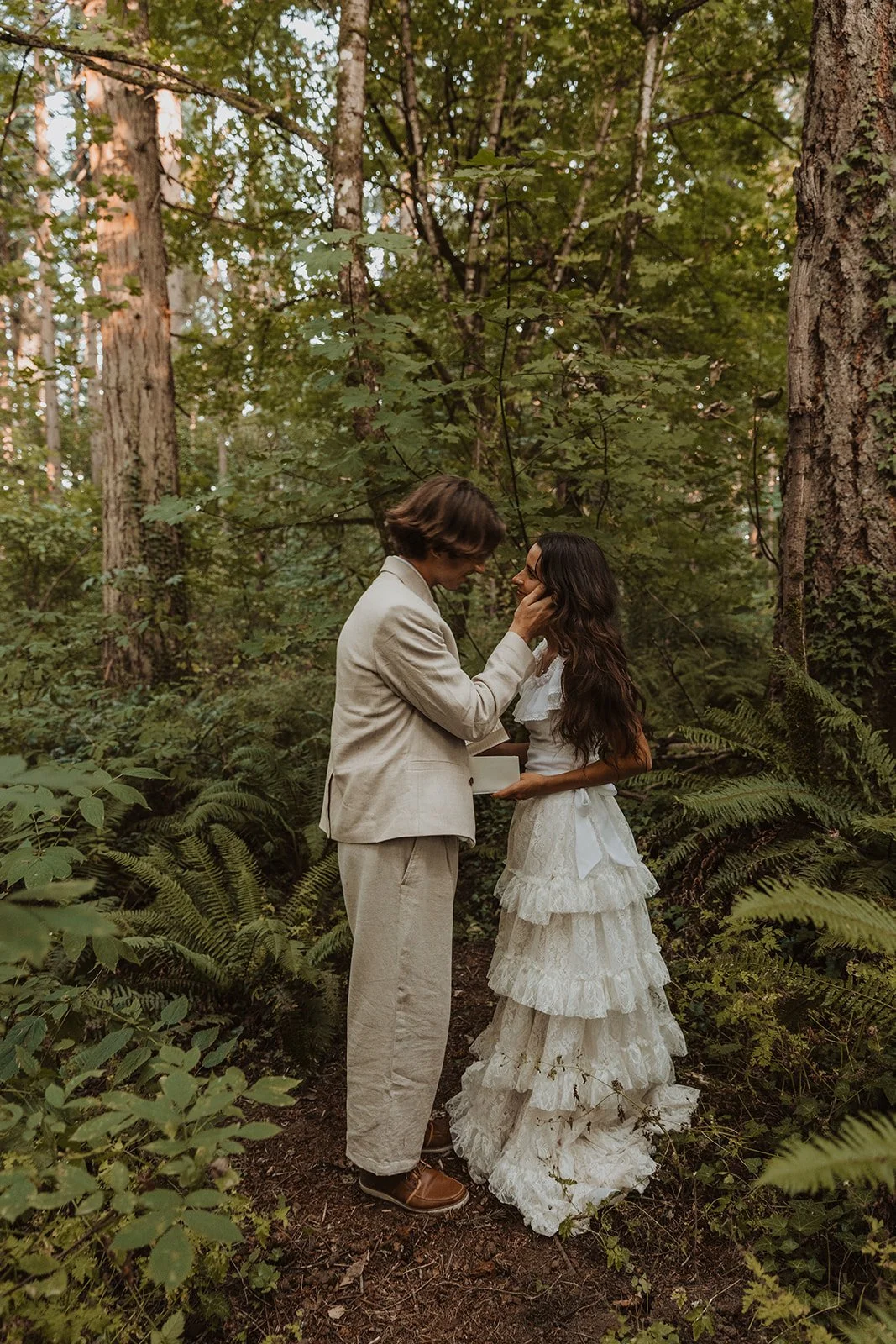 Bride and groom sharing intimate moment surrounded by lush greenery at forest elopement