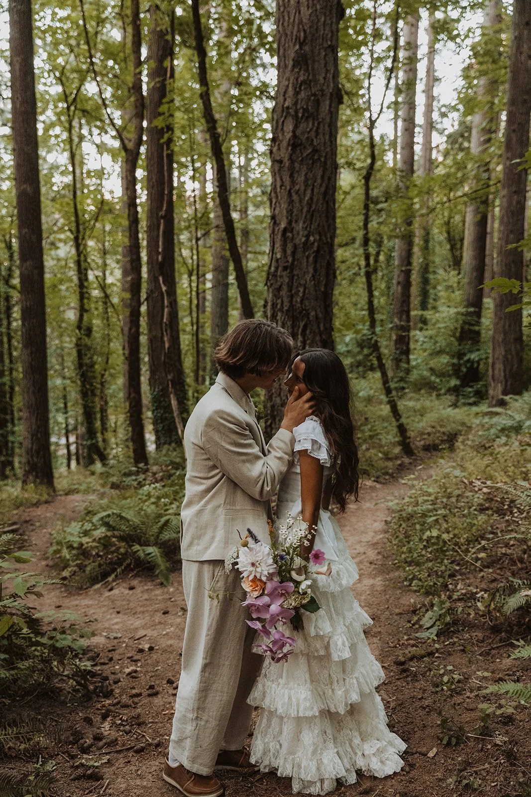 Bride and groom sharing an intimate moment with wildflower bouquet on forest wedding trail