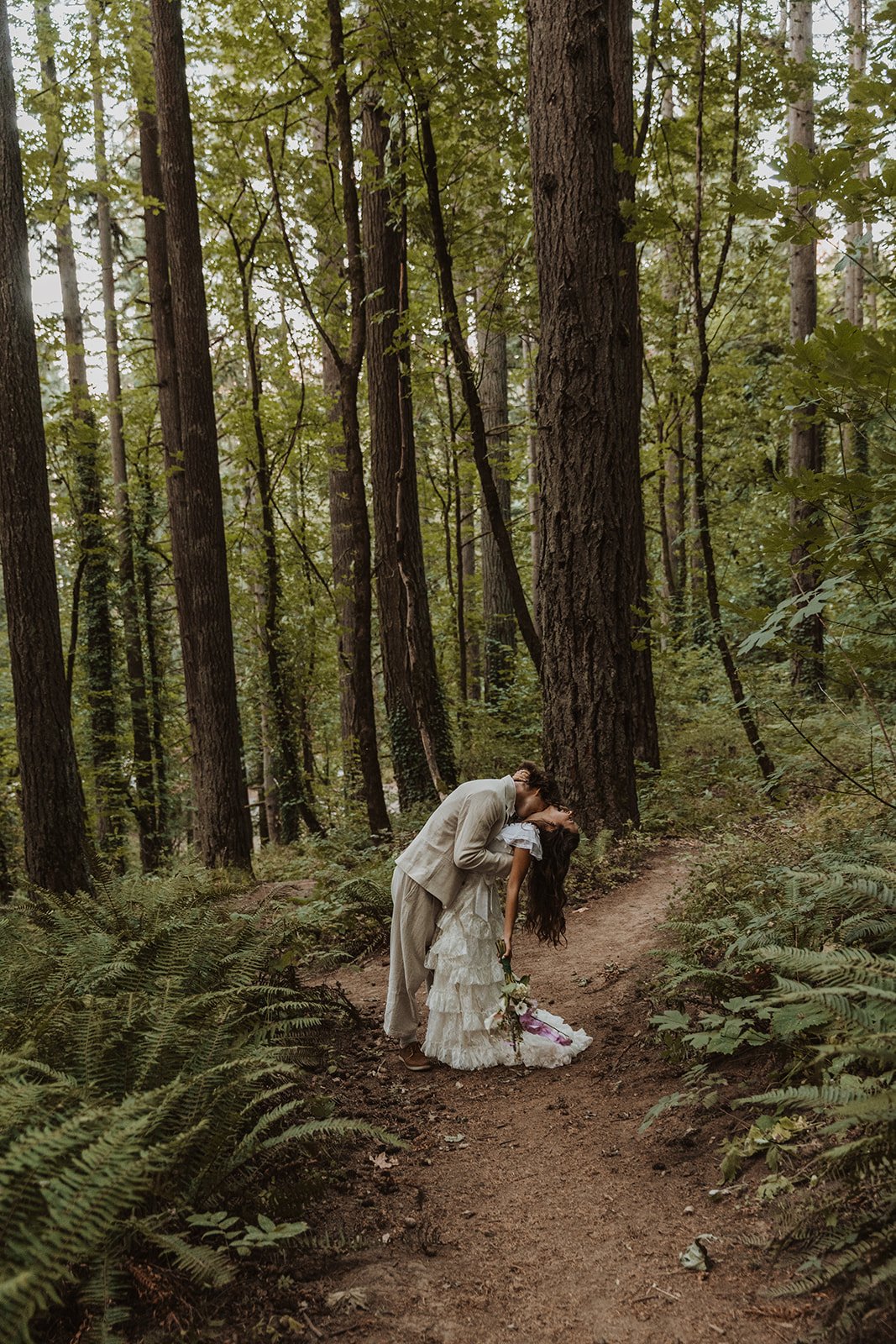 Bride and groom kissing on wooded trail during romantic forest wedding portraits