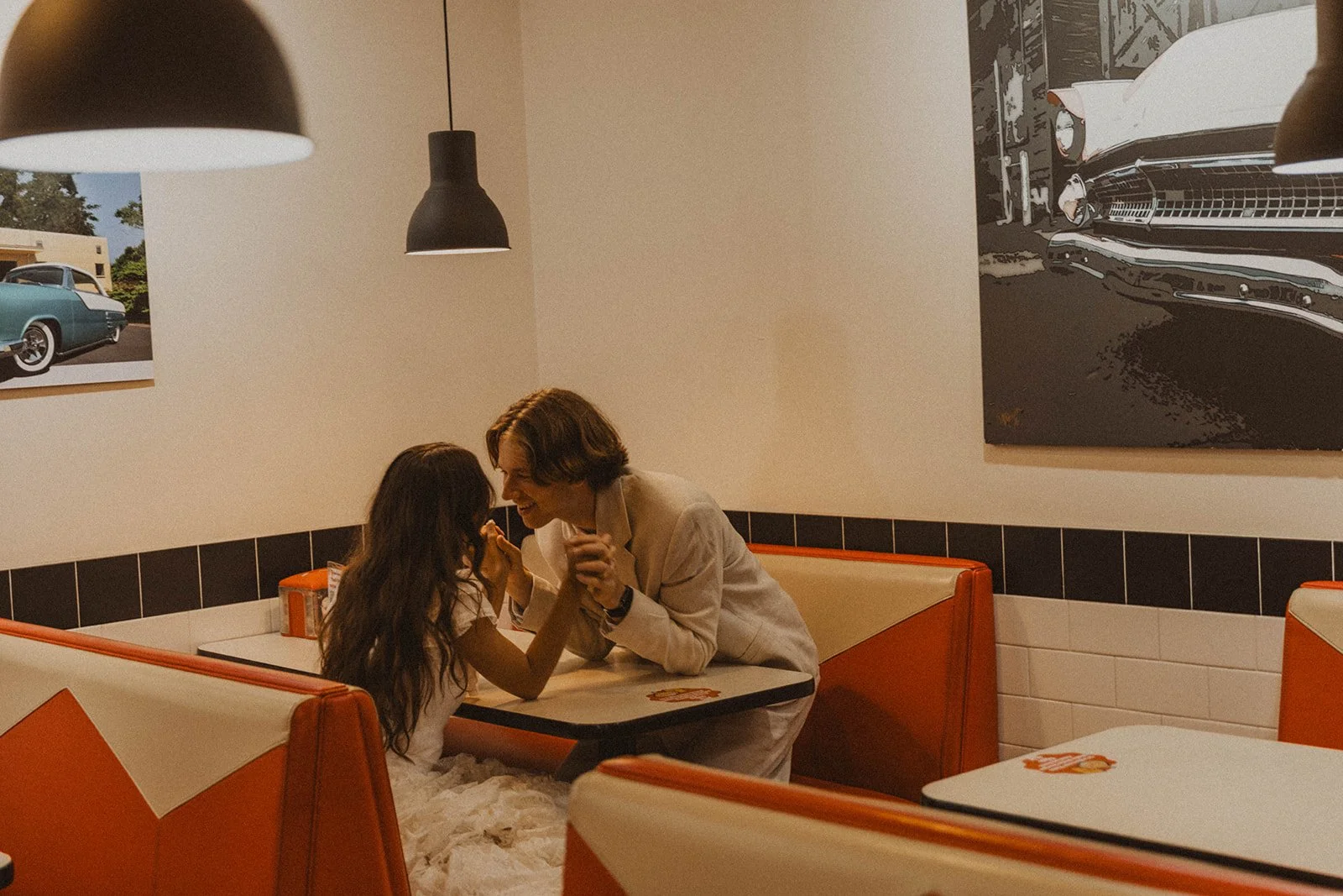 Newlywed couple laughing and holding hands in retro diner booth during intimate wedding night