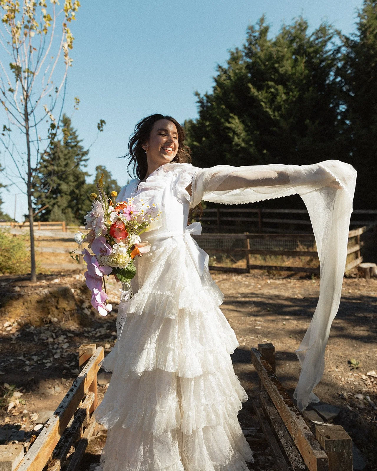 Bride twirling outdoors holding bouquet, flowing sleeves and textured lace wedding dress in sunlight