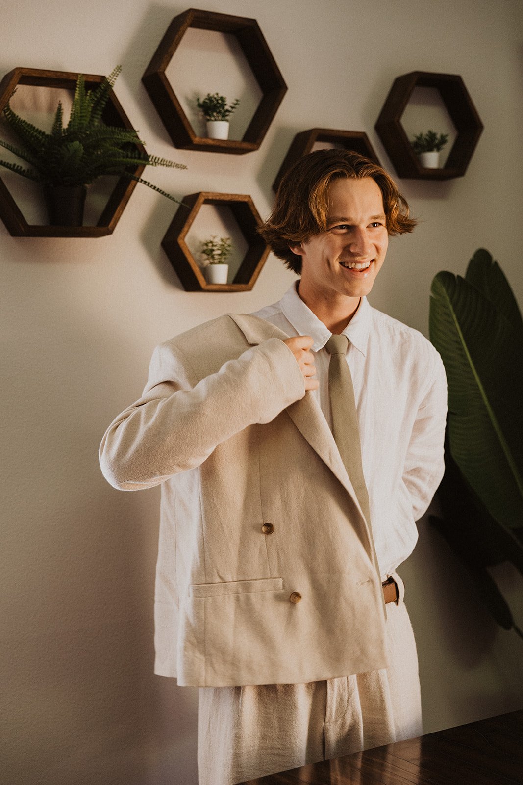 Candid groom getting dressed with neutral suit and tie before wedding ceremony