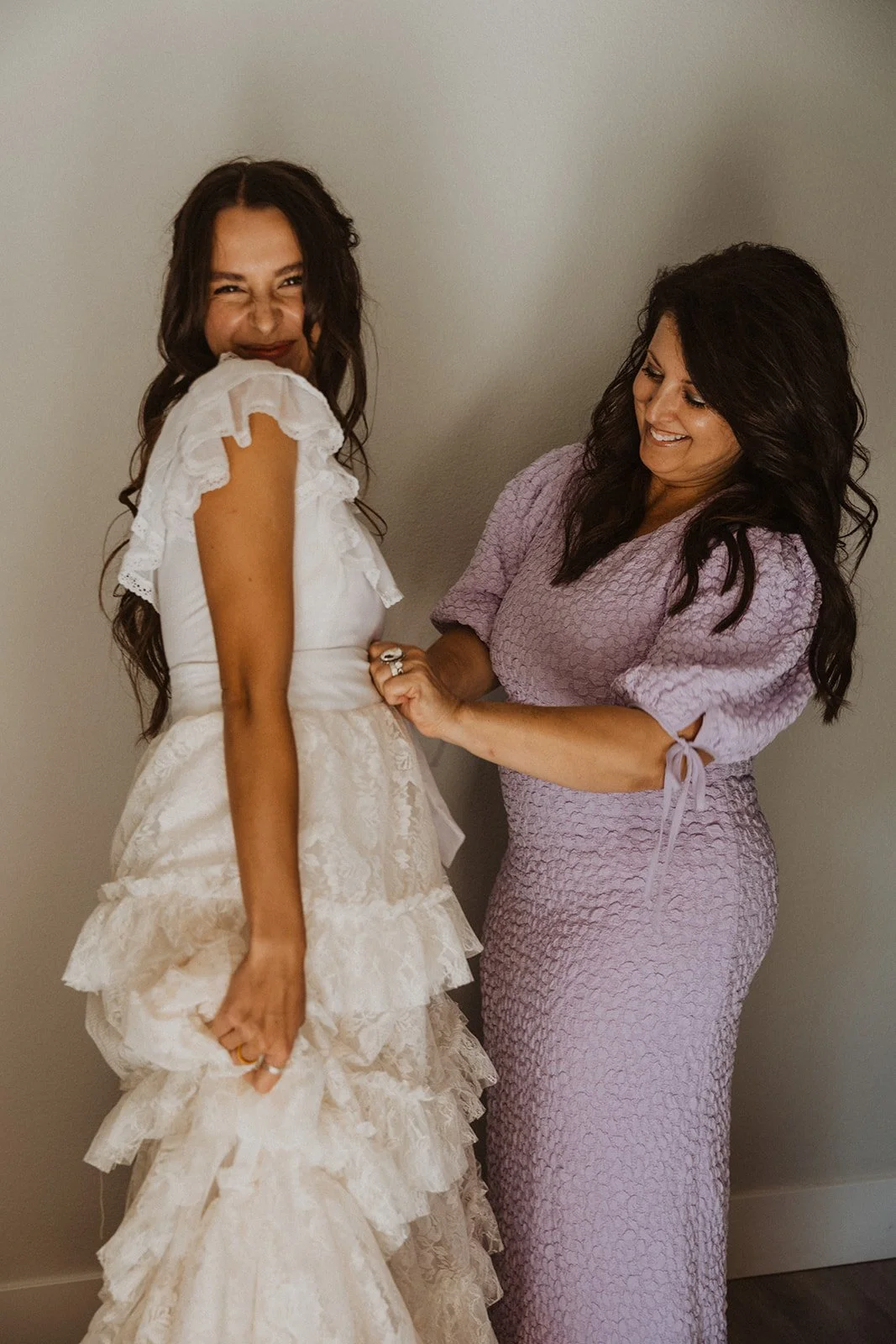 Bride getting ready with assistance from mom tying dress, candid wedding morning moment