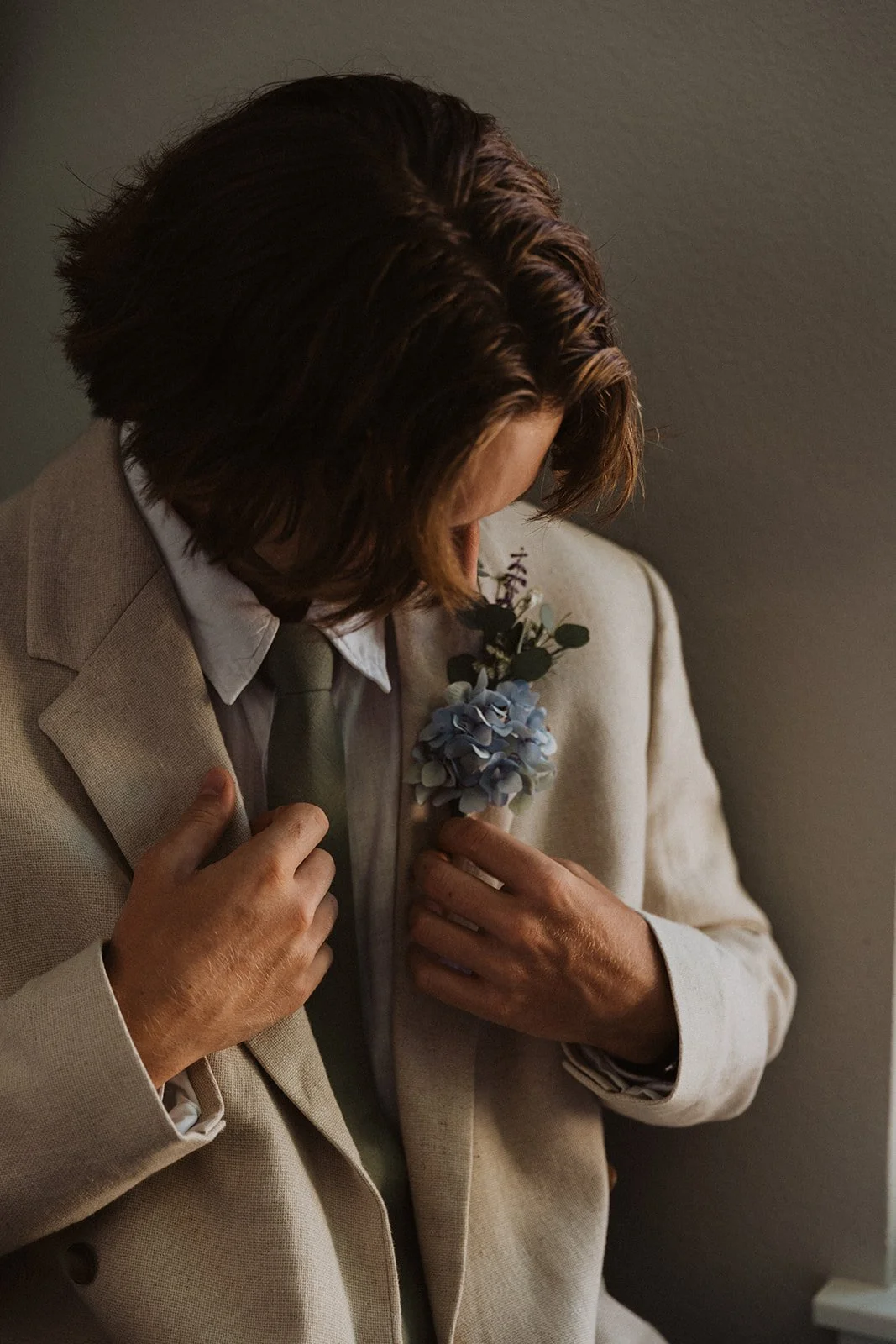 Groom putting on suit jacket while getting ready for wedding indoors