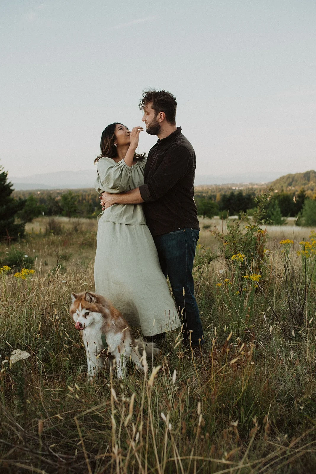 Couple embracing in an open field with their dog during a relaxed Oregon engagement photo session