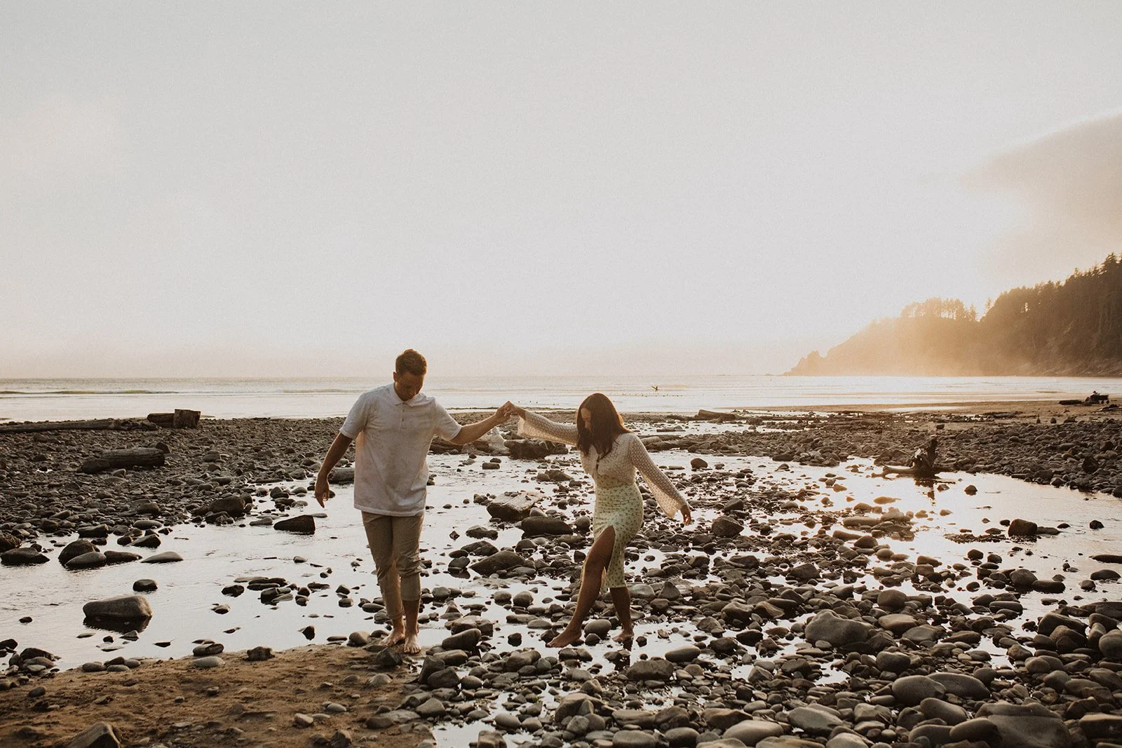 Couple walking barefoot across a rocky beach at sunset during an Oregon coast engagement session