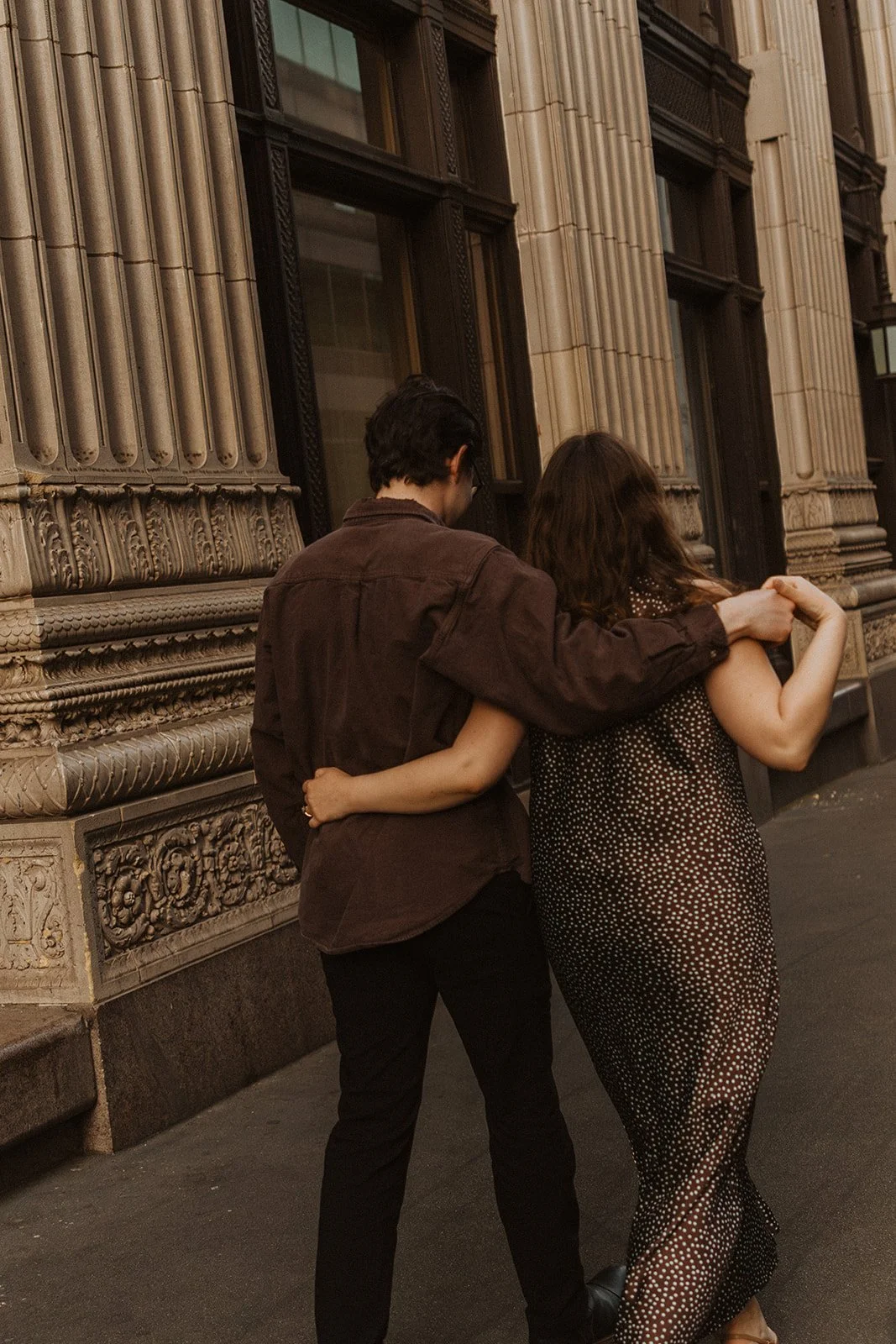 Couple walking arm in arm past a historic building during a Portland engagement session