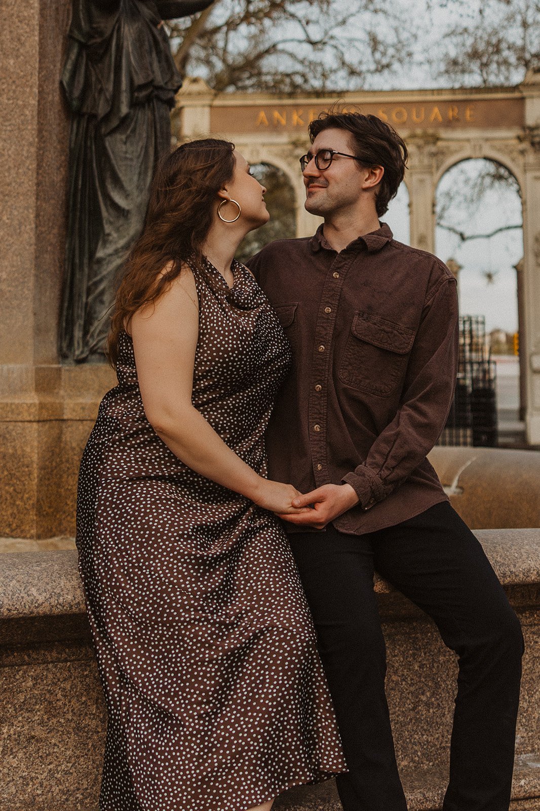 Couple sitting together and holding hands near Ankeny Square during a downtown Portland engagement session