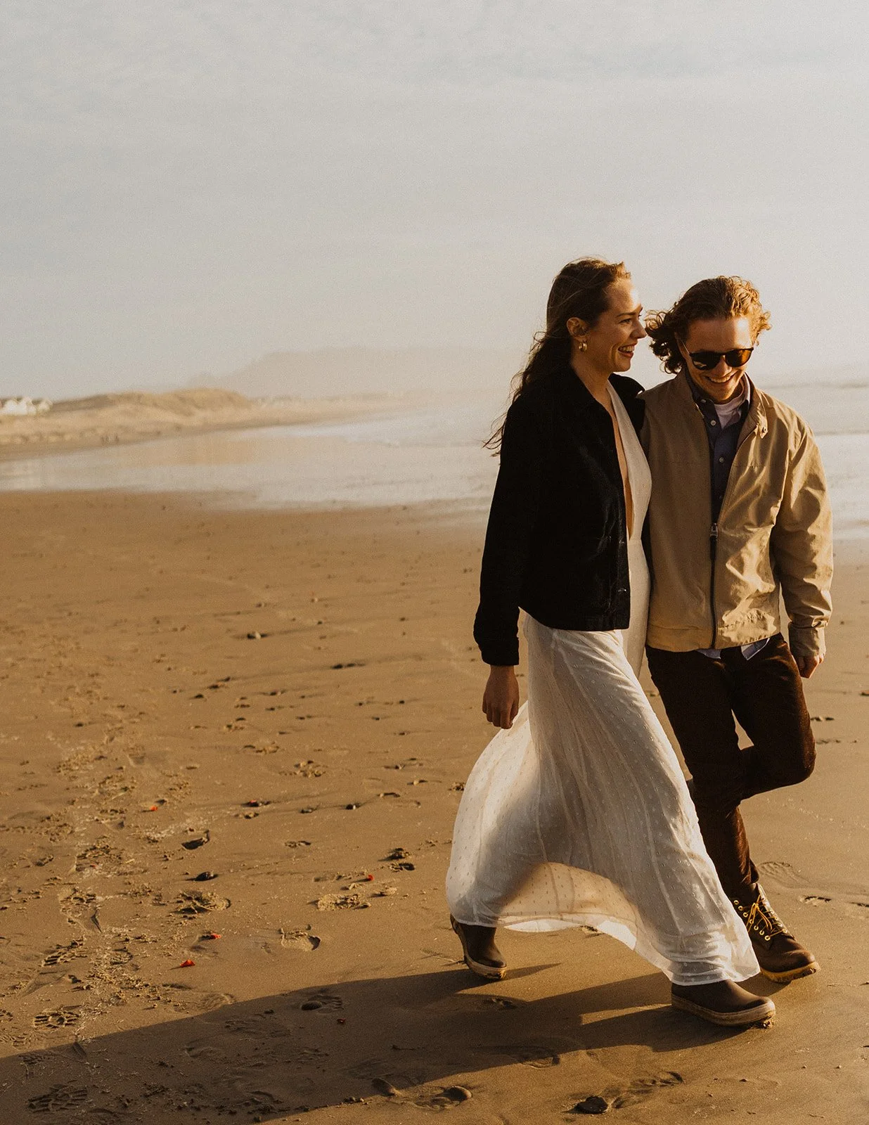 Couple walking along the beach at sunset on the Oregon Coast, smiling and enjoying a relaxed engagement session