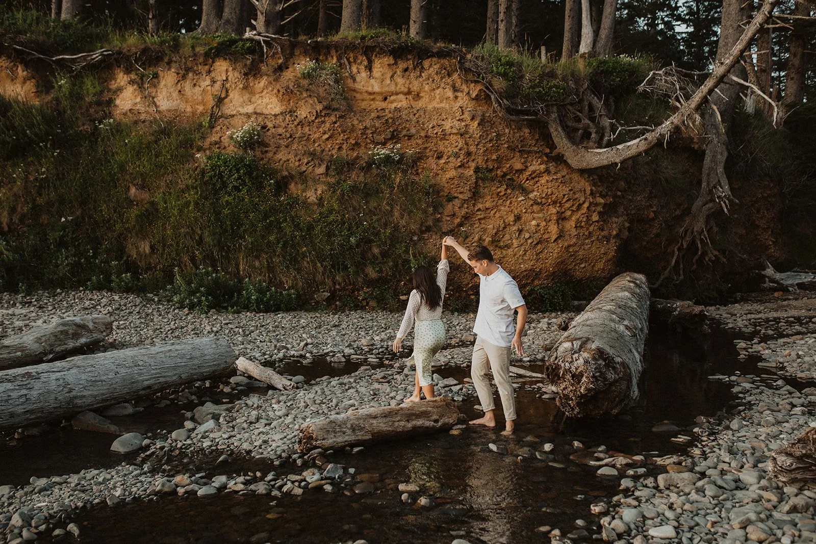 Couple laughing during a piggyback ride on a rocky beach with driftwood along the Oregon Coast at golden hour