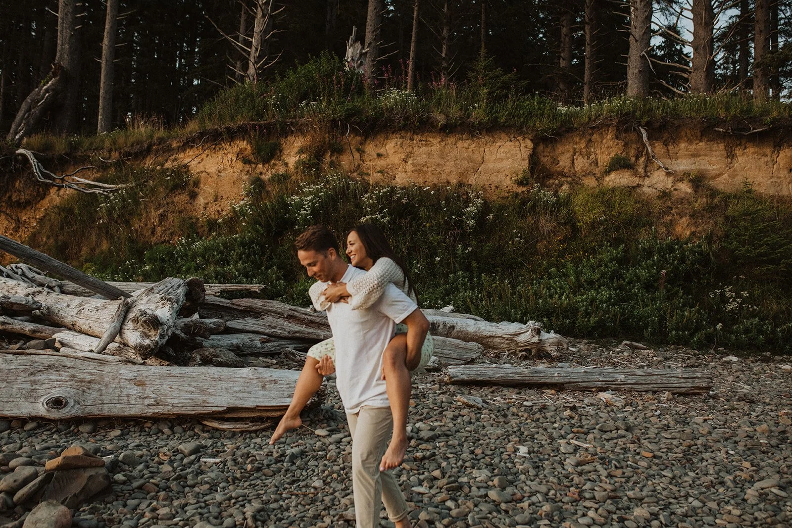 Couple holding hands while walking barefoot across a rocky creek with driftwood along the Oregon Coast