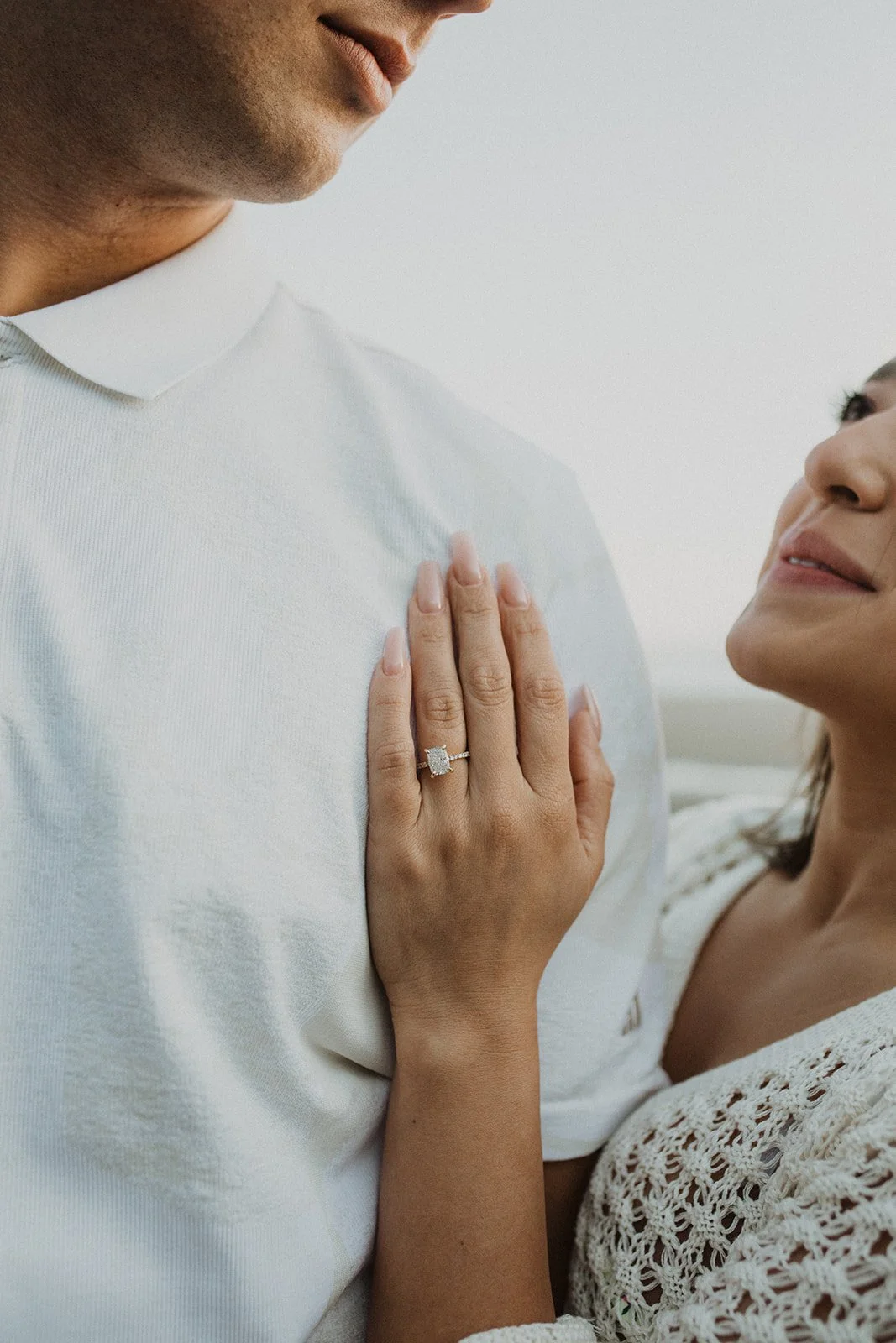 Close-up of engagement ring on woman’s hand resting on partner’s chest during a beach engagement session