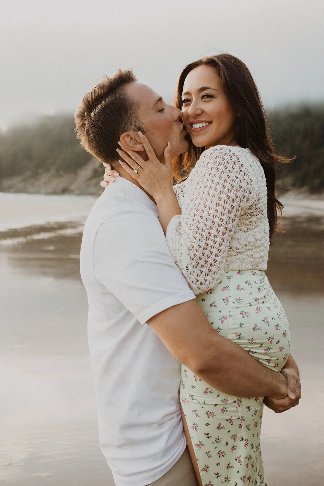 Man kissing woman on the cheek during a romantic Oregon coast engagement session on a sandy beach