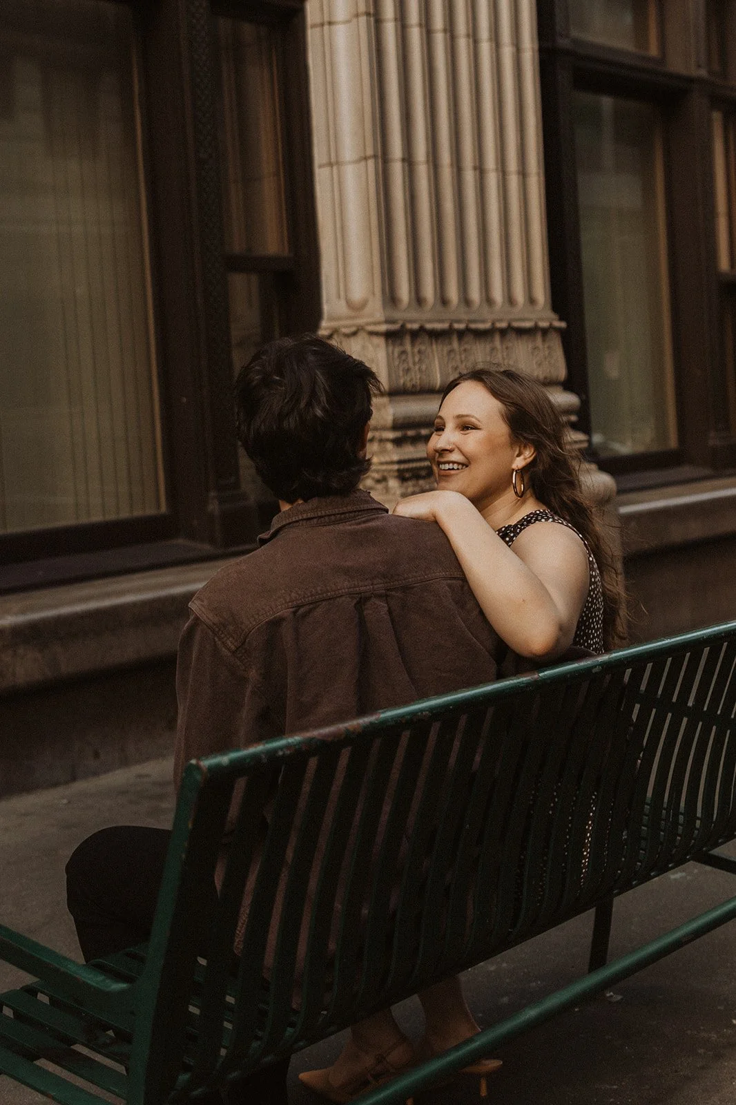 Couple laughing together while sitting on a bench during a relaxed downtown city engagement session
