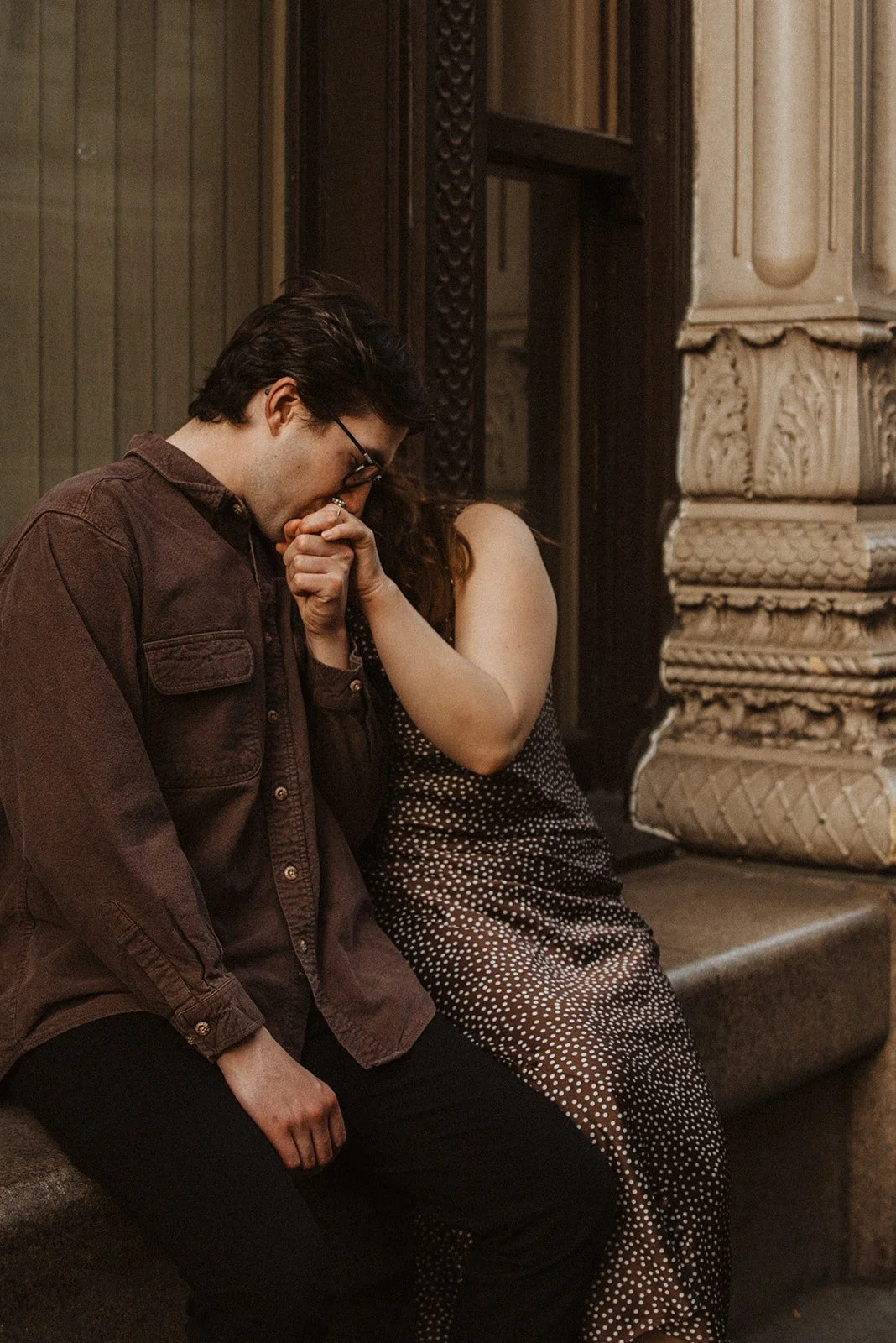 Man kissing woman’s hand during an intimate urban engagement session outside a downtown building
