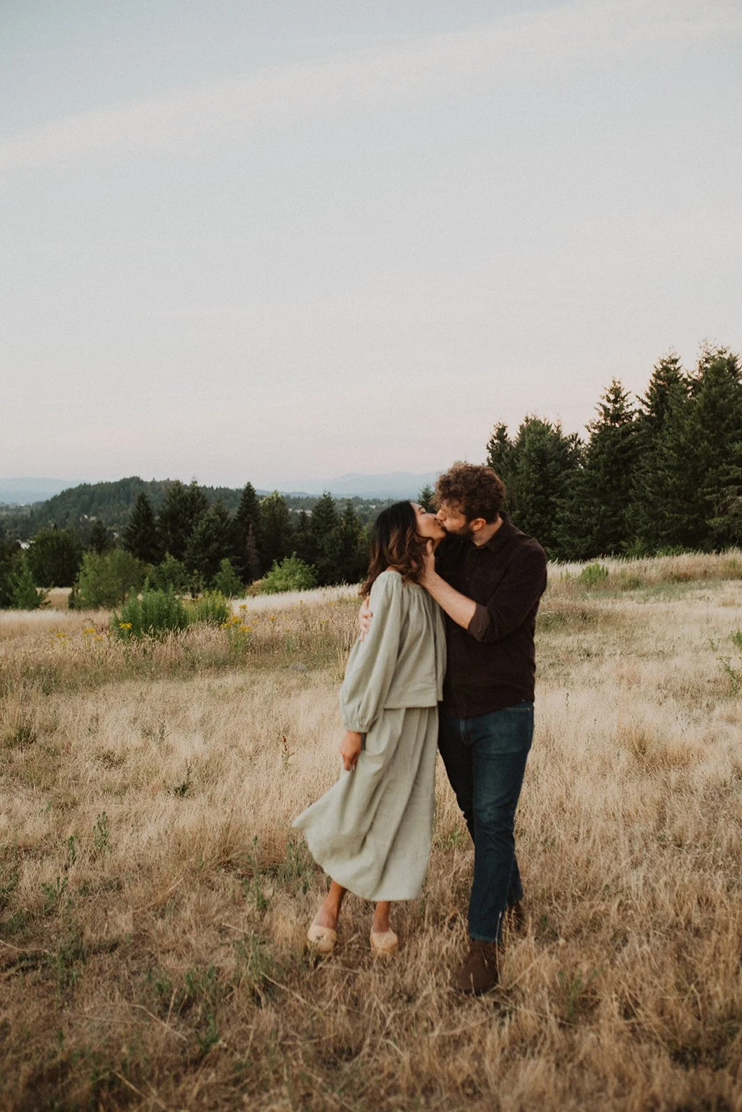 Couple kissing in an open meadow field during a romantic Oregon engagement session with soft natural light