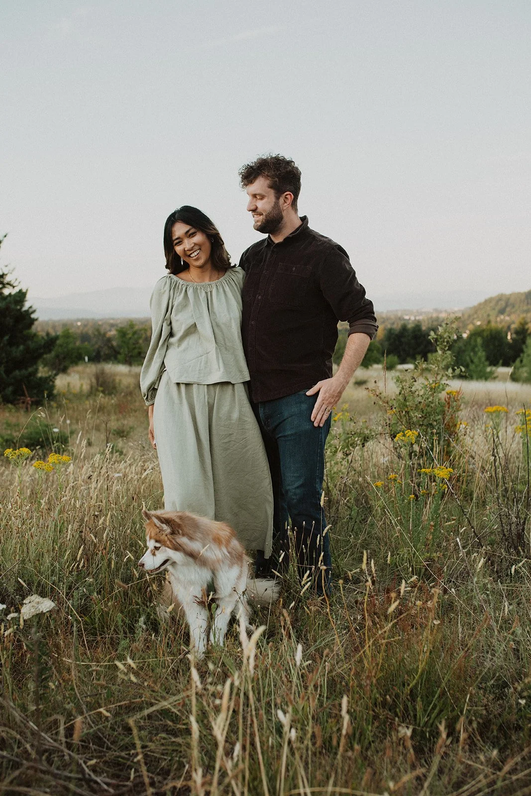 Couple walking with their dog through a grassy meadow during a relaxed outdoor engagement session in Oregon