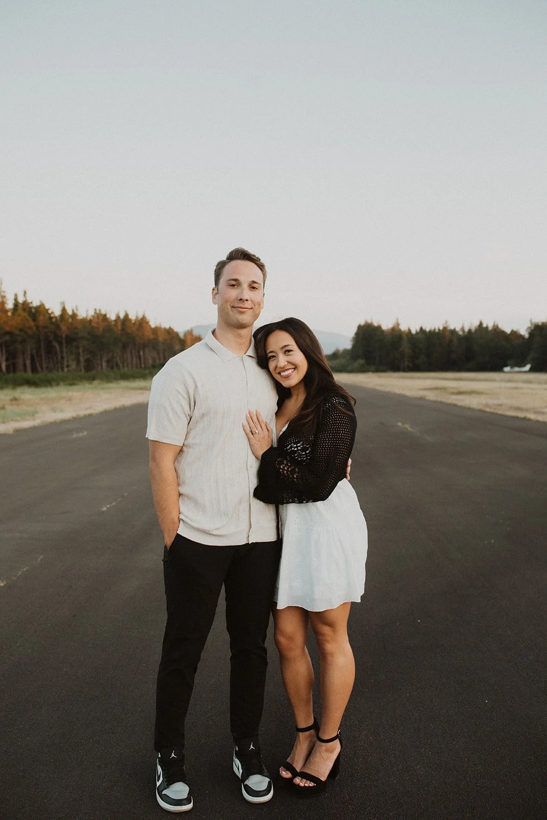 Couple standing together on an open road during an outdoor engagement session, smiling and embracing
