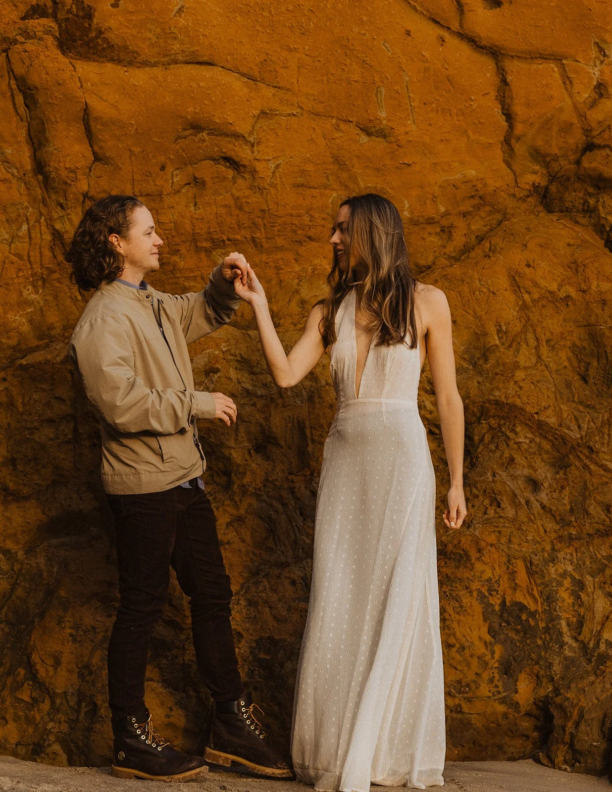 Couple holding hands and playfully pulling each other along a rocky Oregon coast cliff during an engagement session