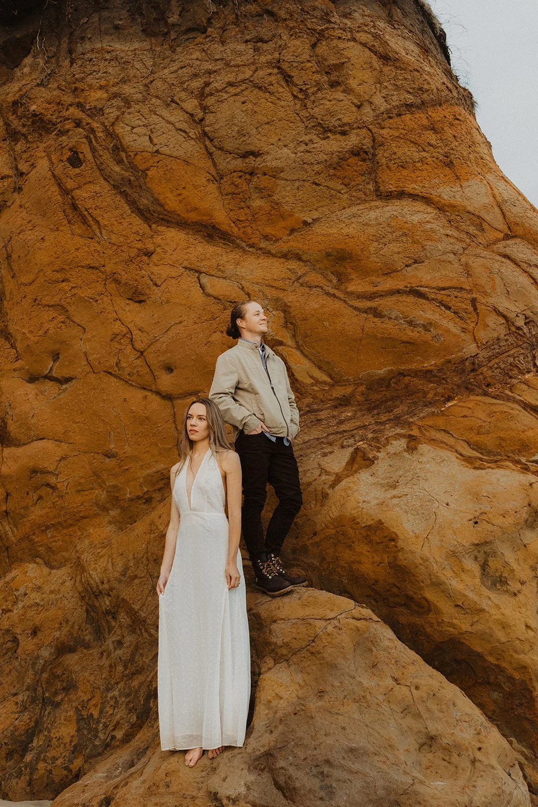 Couple standing on a rocky cliffside during an Oregon coast engagement session with dramatic natural backdrop