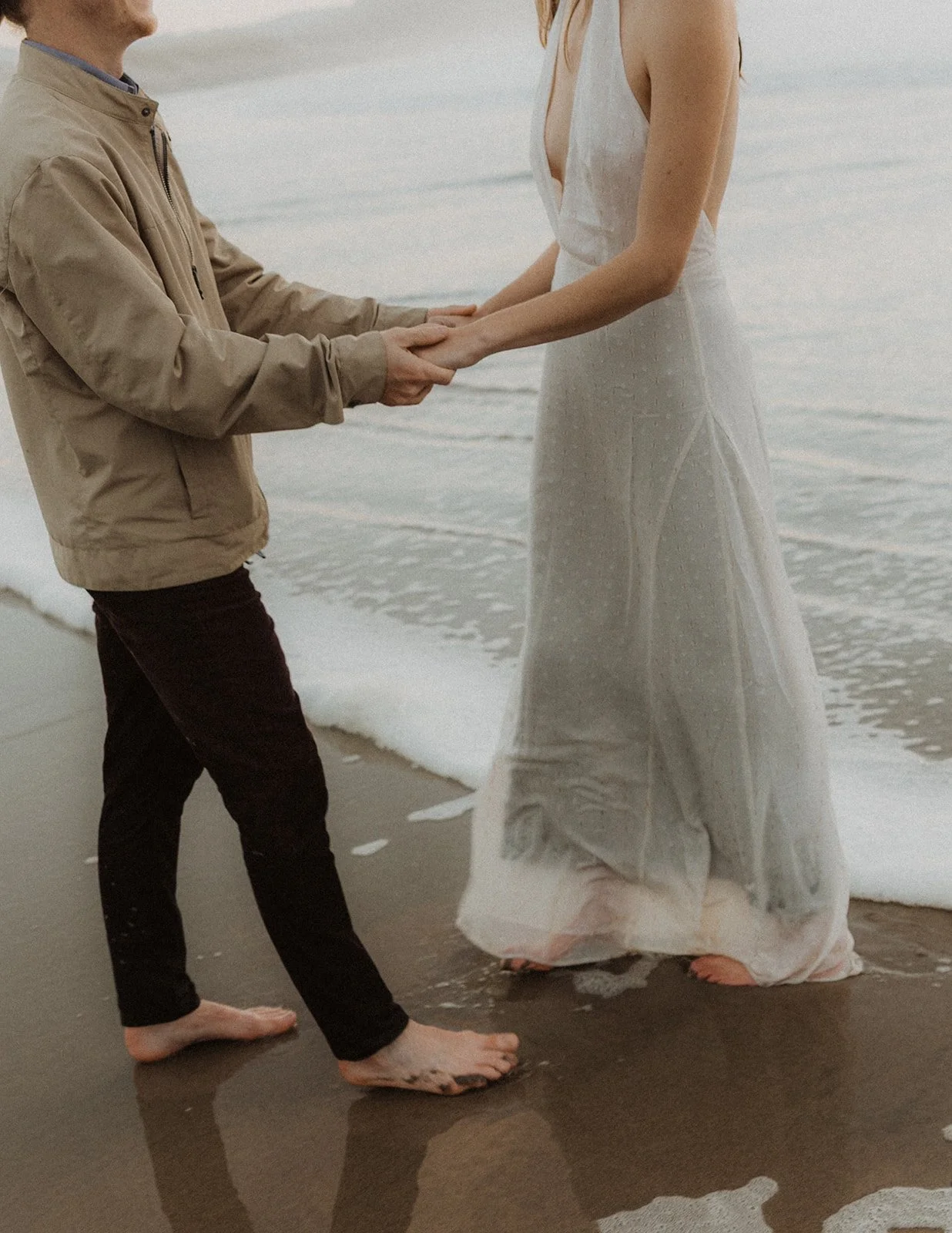 Couple holding hands barefoot at the shoreline with ocean waves during an Oregon coast engagement session