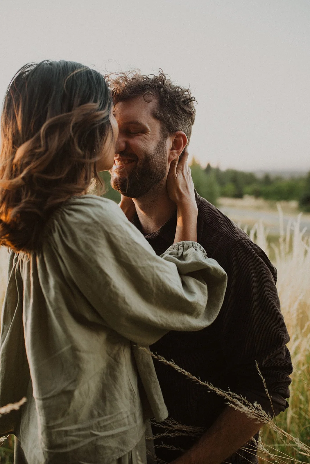 Close-up of couple sharing a kiss in a grassy field during golden hour engagement session with soft natural light