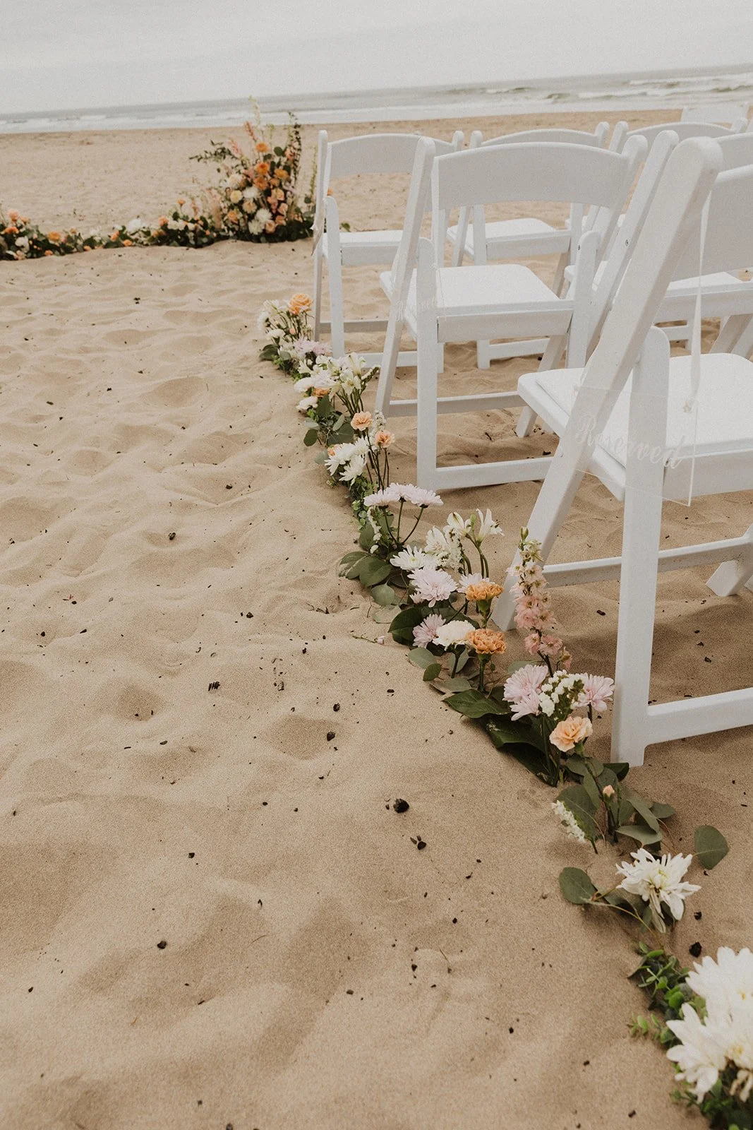 Floral-lined sandy aisle and white ceremony chairs set up for an intimate Cannon Beach wedding ceremony