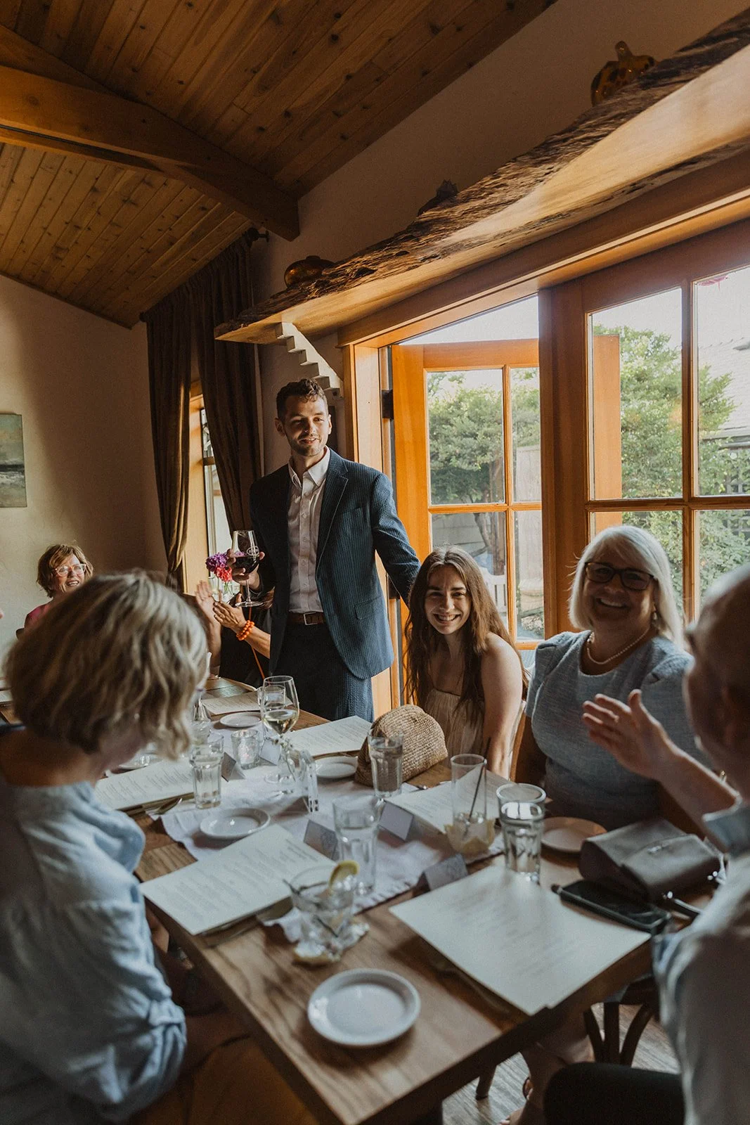 Couple laughing with friends and family during an intimate rehearsal dinner before their Cannon Beach wedding weekend