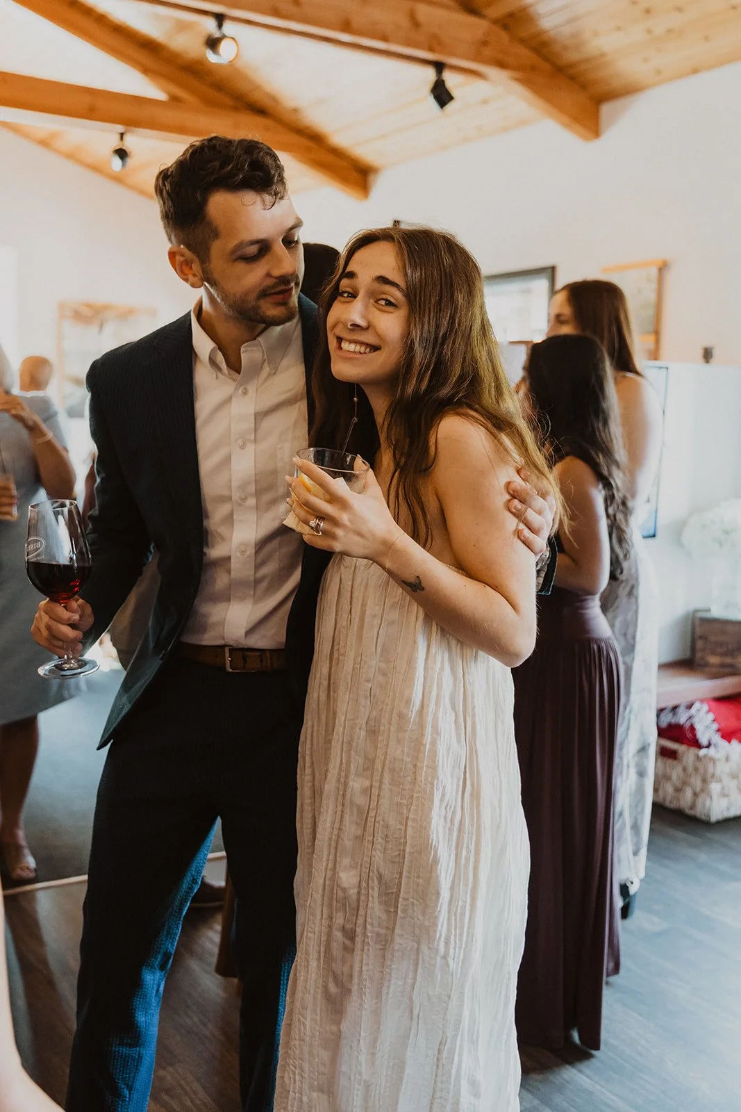 Candid moment of the couple embracing during their laid-back Cannon Beach wedding celebration indoors with guests nearby