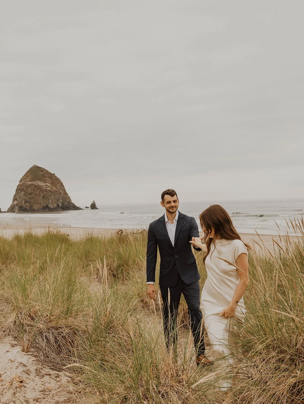 Newly married couple walking hand in hand through beach dunes during their Cannon Beach wedding portraits