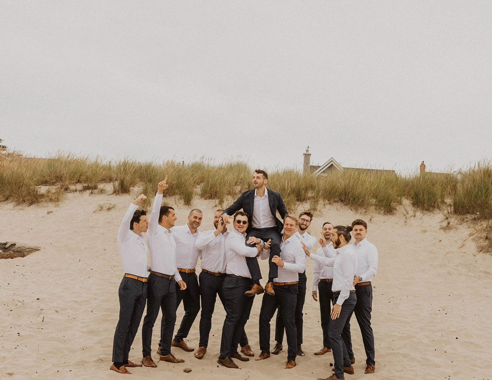 Groomsmen celebrating and lifting the groom on the beach after an Oregon coast wedding ceremony