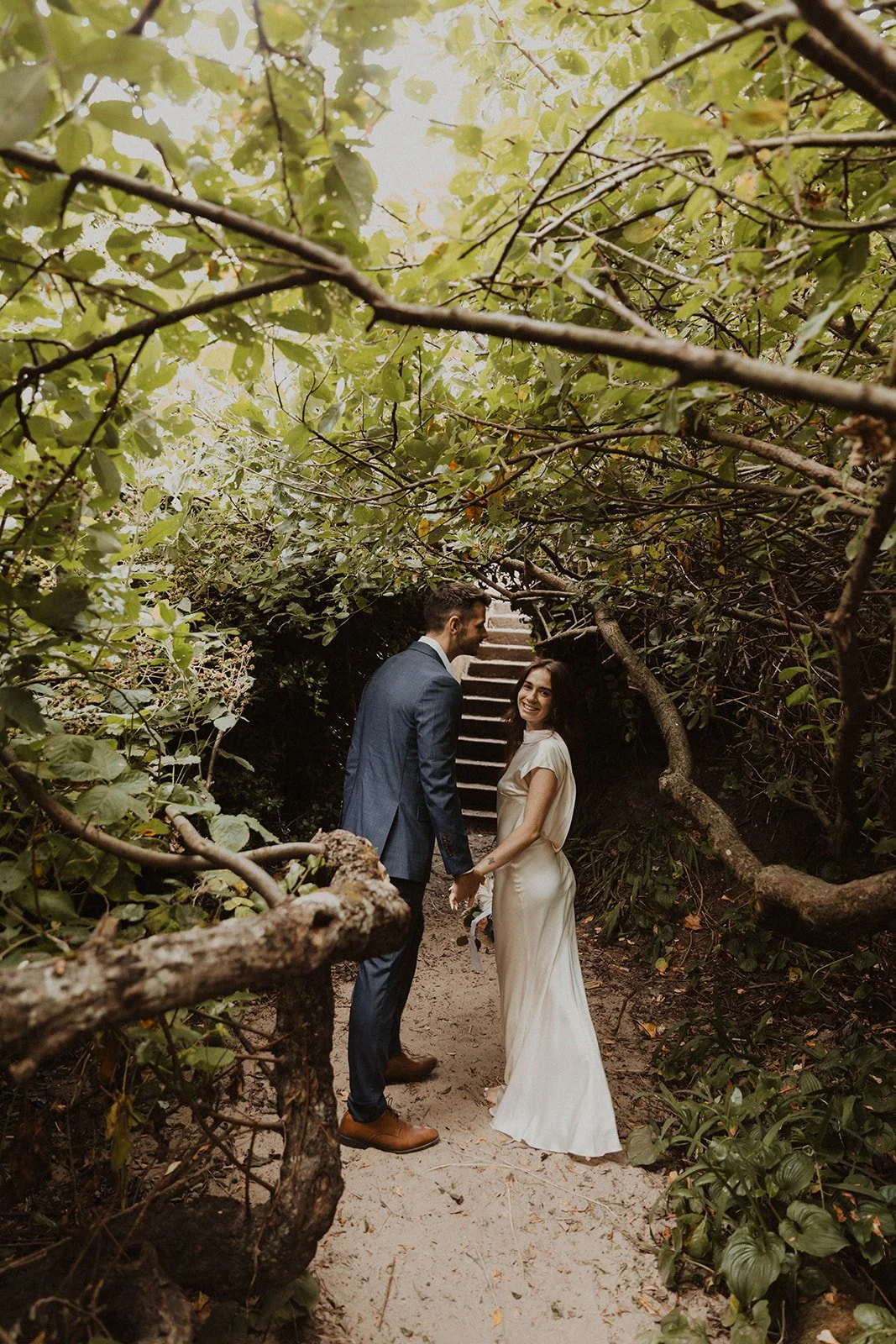 Newlywed couple walking hand in hand through a lush forest path near Cannon Beach during their intimate coastal wedding portraits