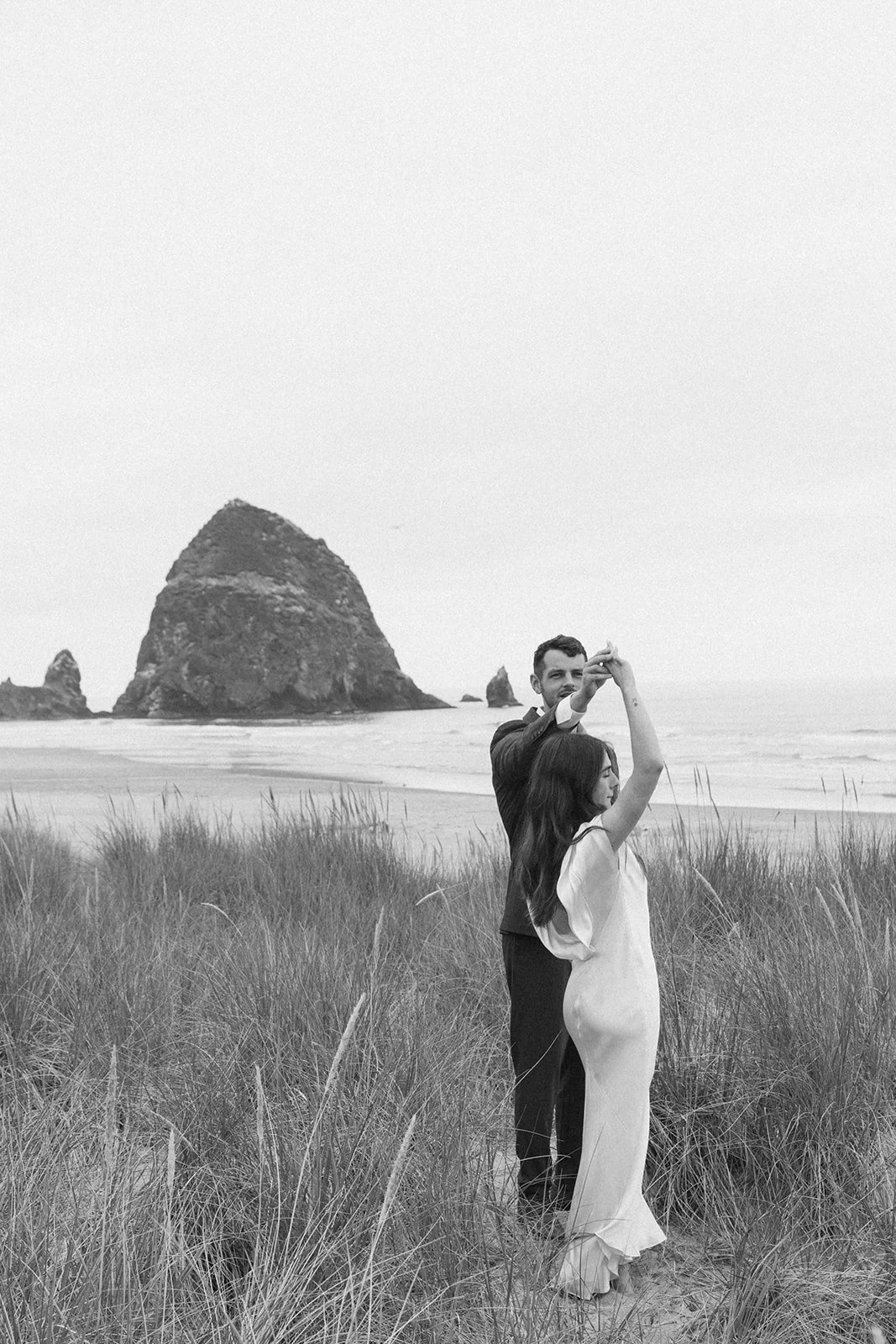 Black and white portrait of a bride and groom dancing together in the dunes near Haystack Rock