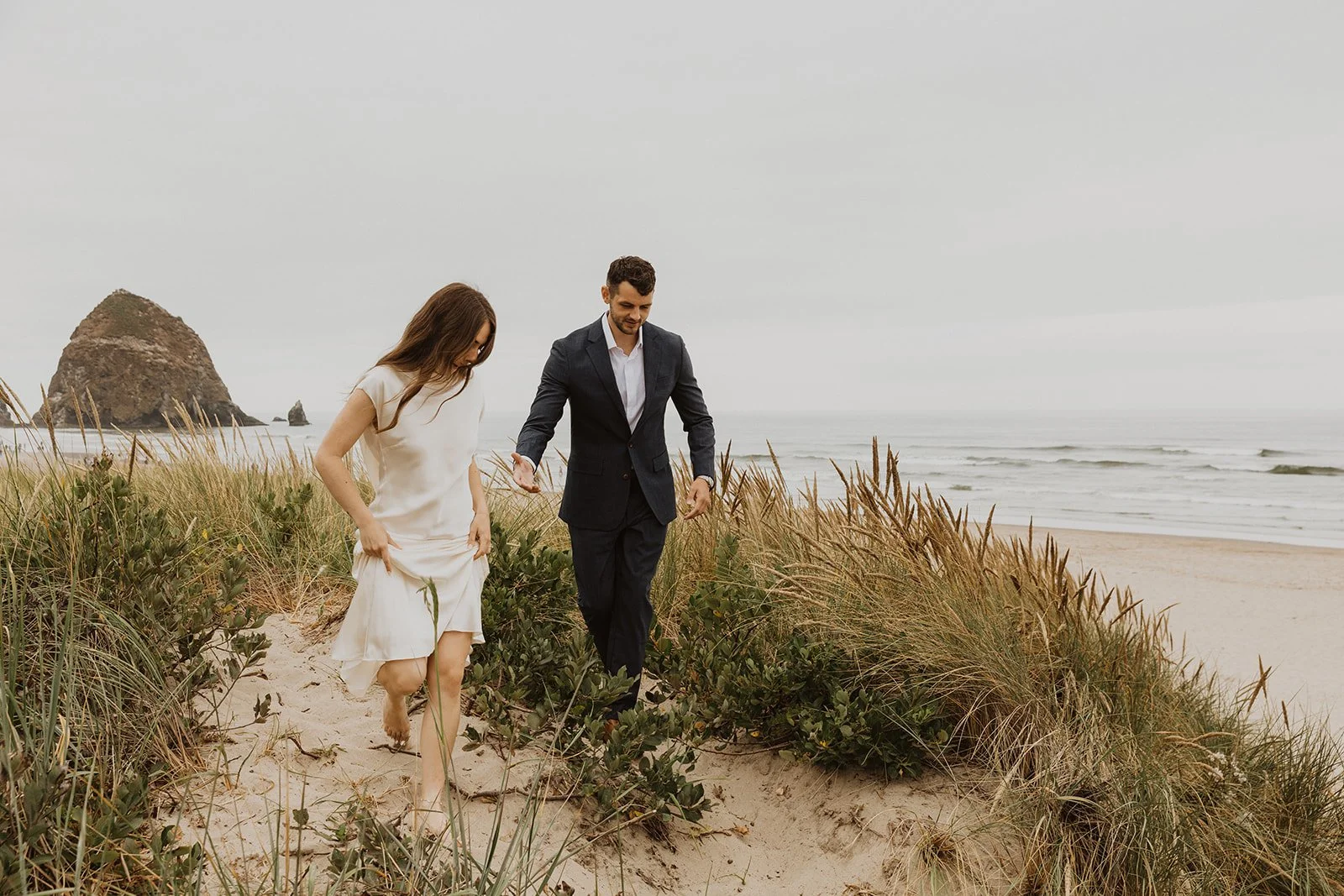 Newlywed couple walking through the grassy dunes near Cannon Beach after their intimate beach elopement ceremony