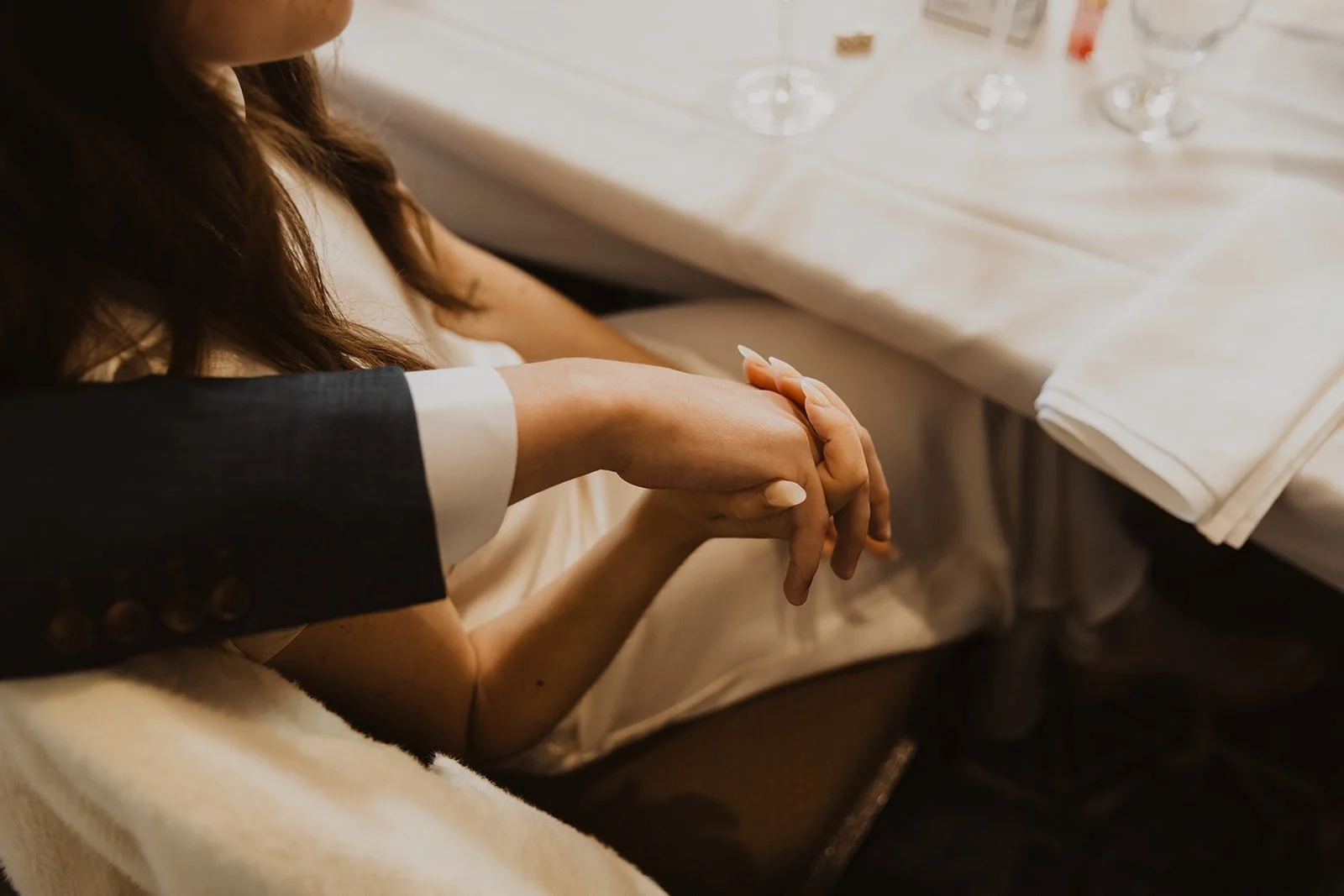 Close-up detail of a newlywed couple holding hands during their candlelit wedding reception dinner
