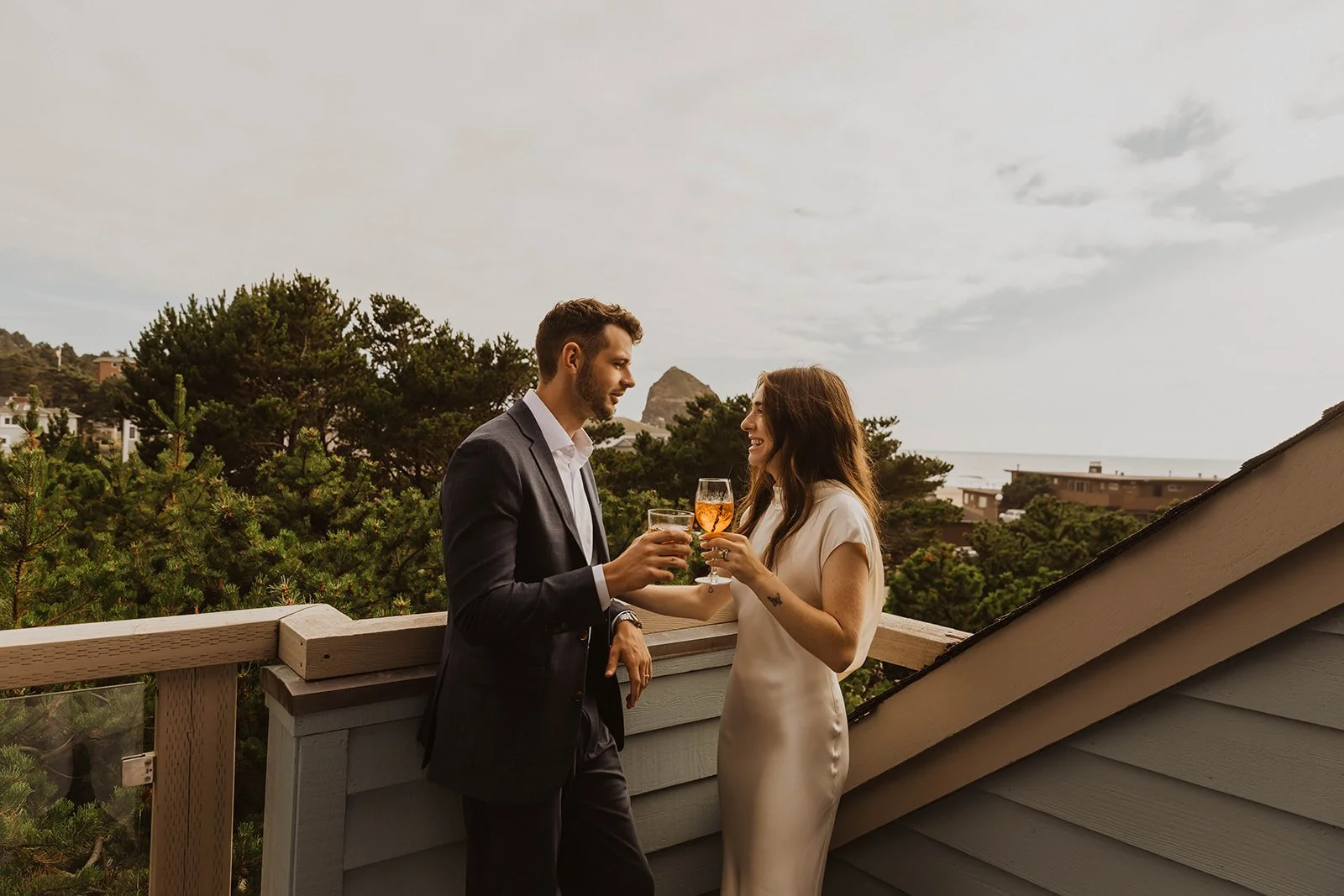 Newlywed couple sharing cocktails together on a balcony overlooking the Oregon coast