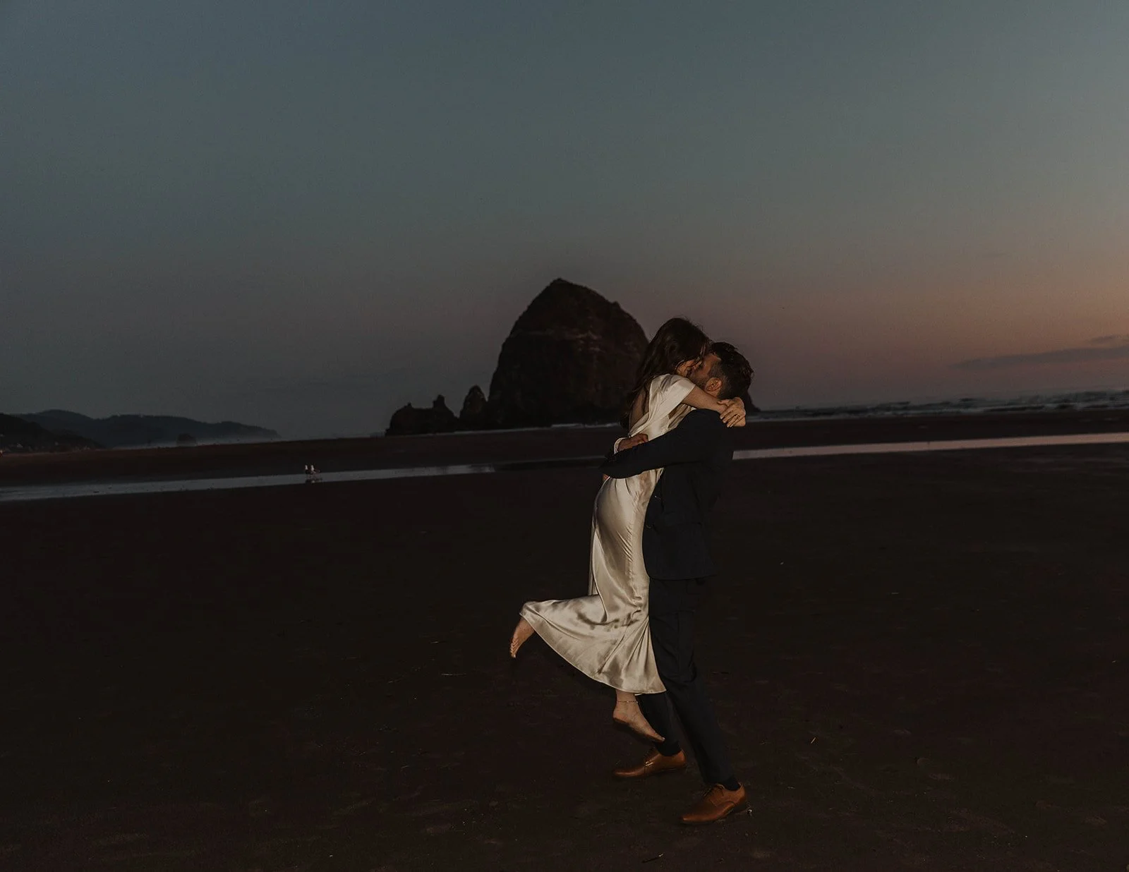 Groom lifting bride during a playful sunset moment on the Oregon coast