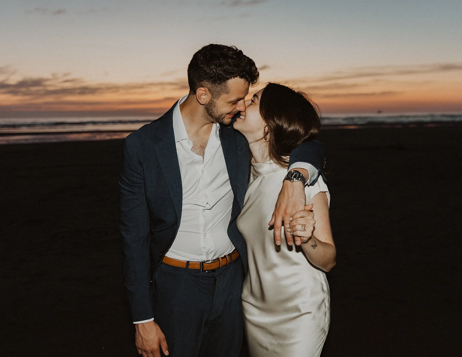 Newlywed couple embracing and smiling together on Cannon Beach at sunset after their intimate wedding