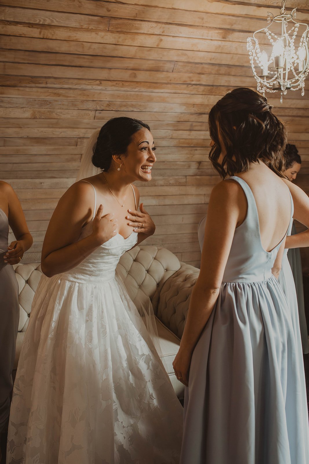 Bride sharing an emotional and excited moment with a bridesmaid during wedding morning preparations in a softly lit bridal suite.