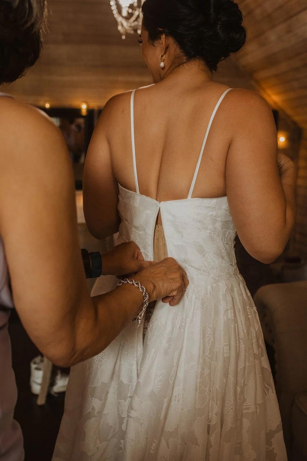 Close-up of the bride’s wedding dress being buttoned during getting-ready moments inside a softly lit bridal suite.