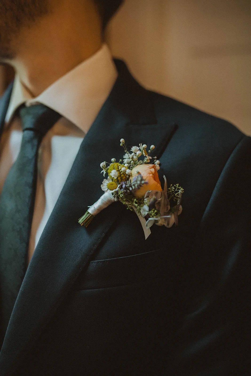 Close-up detail of a groom’s boutonniere with peach roses and wildflowers pinned to a dark navy wedding suit jacket.
