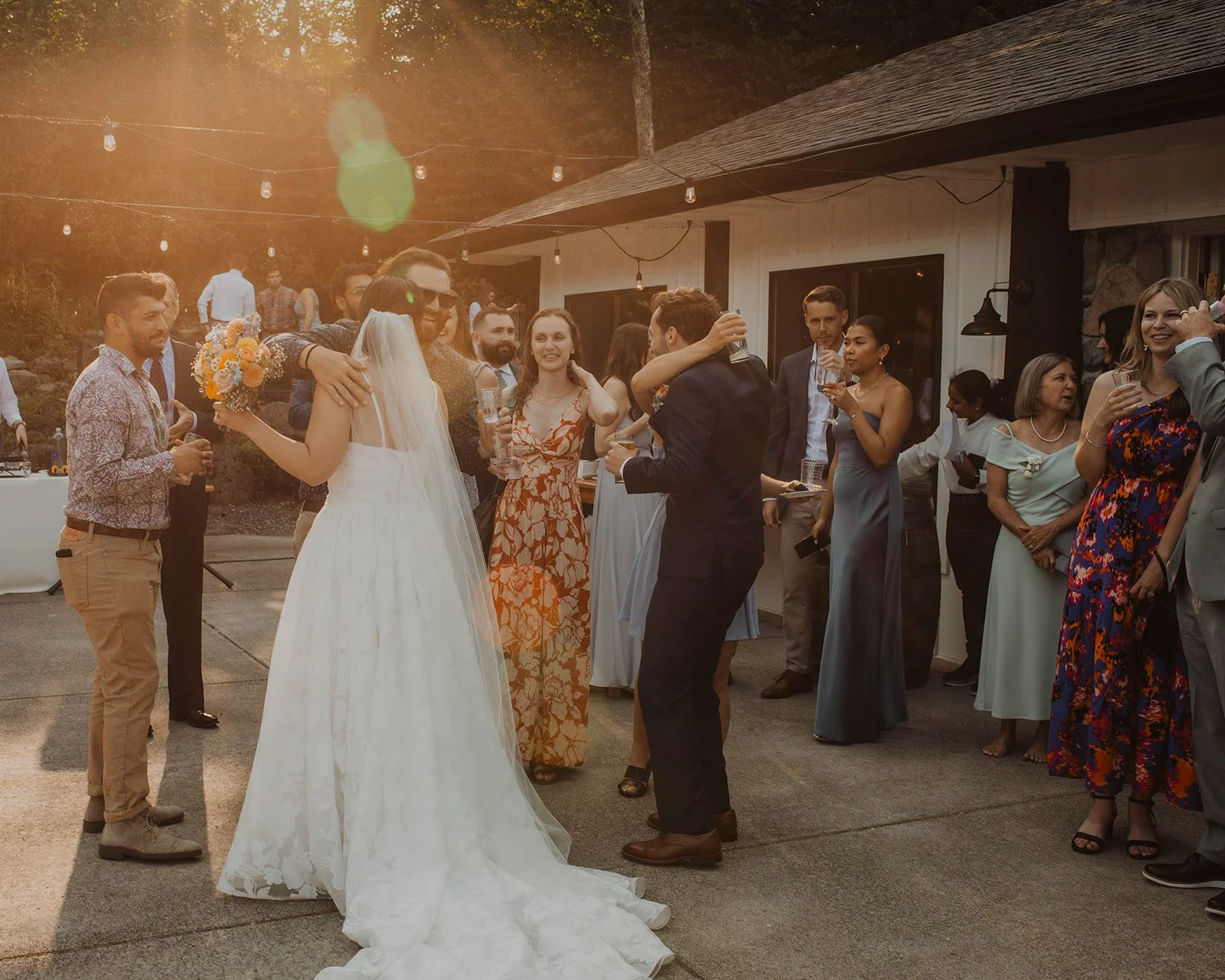 Bride and groom laughing and mingling with wedding guests during outdoor cocktail hour surrounded by hydrangeas and string lights at the reception venue.