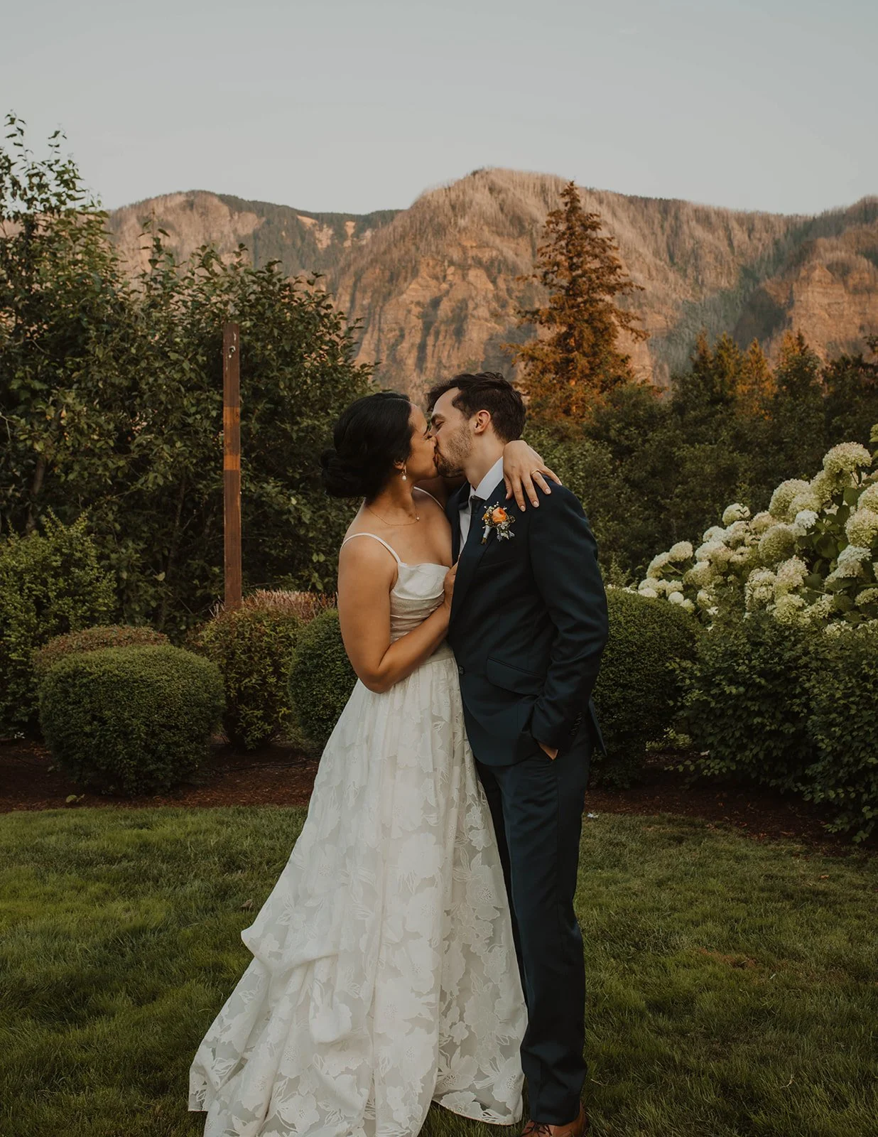 Newlywed couple walking hand in hand through a lush garden path beneath string lights after their outdoor wedding ceremony.