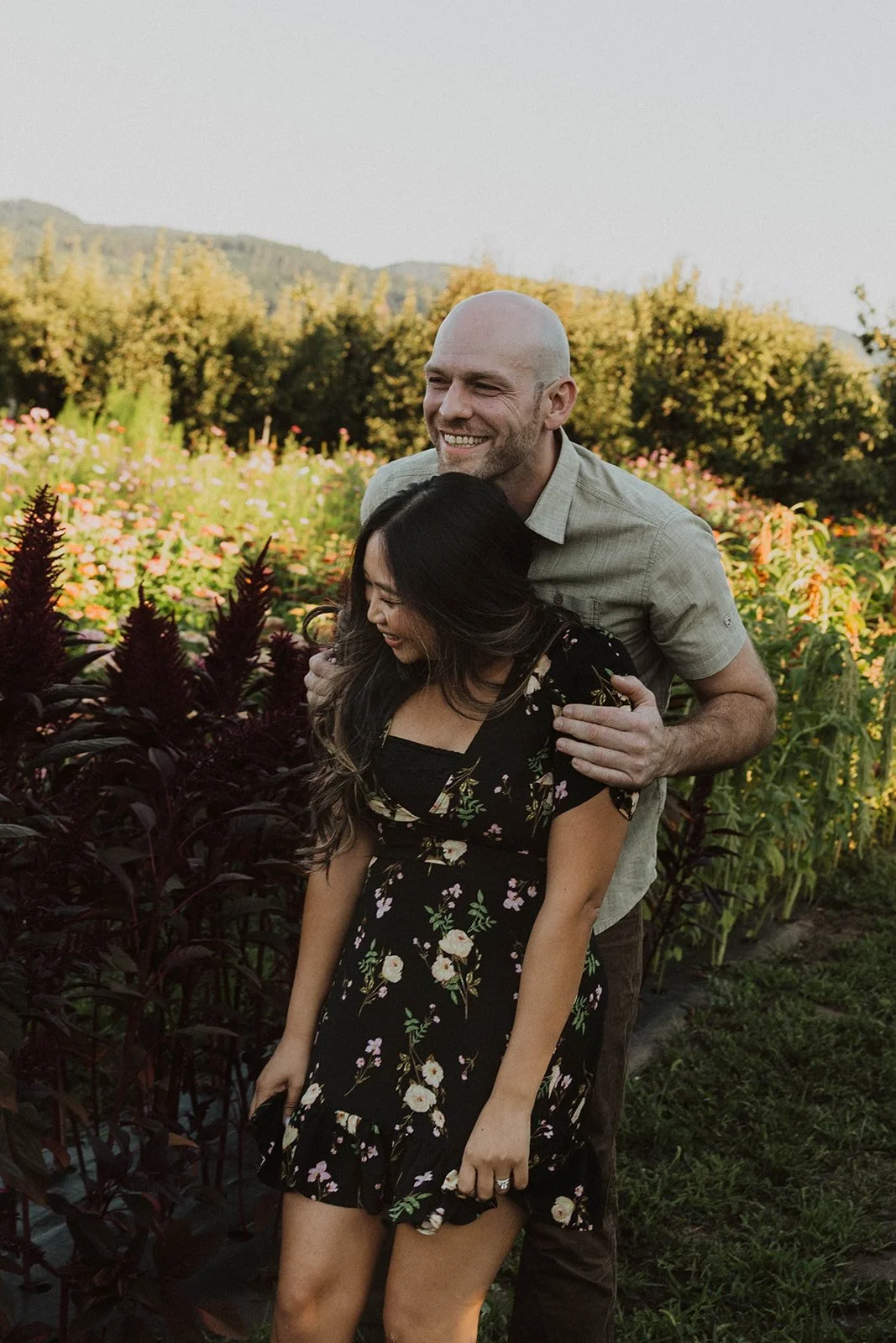 Couple laughing together during a candid engagement session surrounded by blooming flowers and mountain views