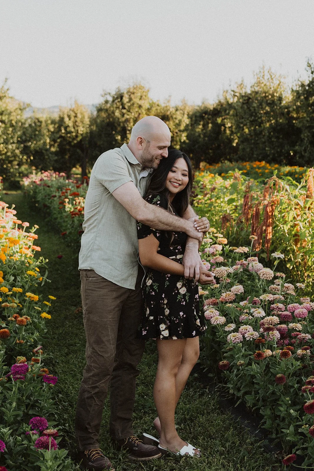 Engaged couple sharing a quiet embrace between rows of blooming zinnias at a flower farm