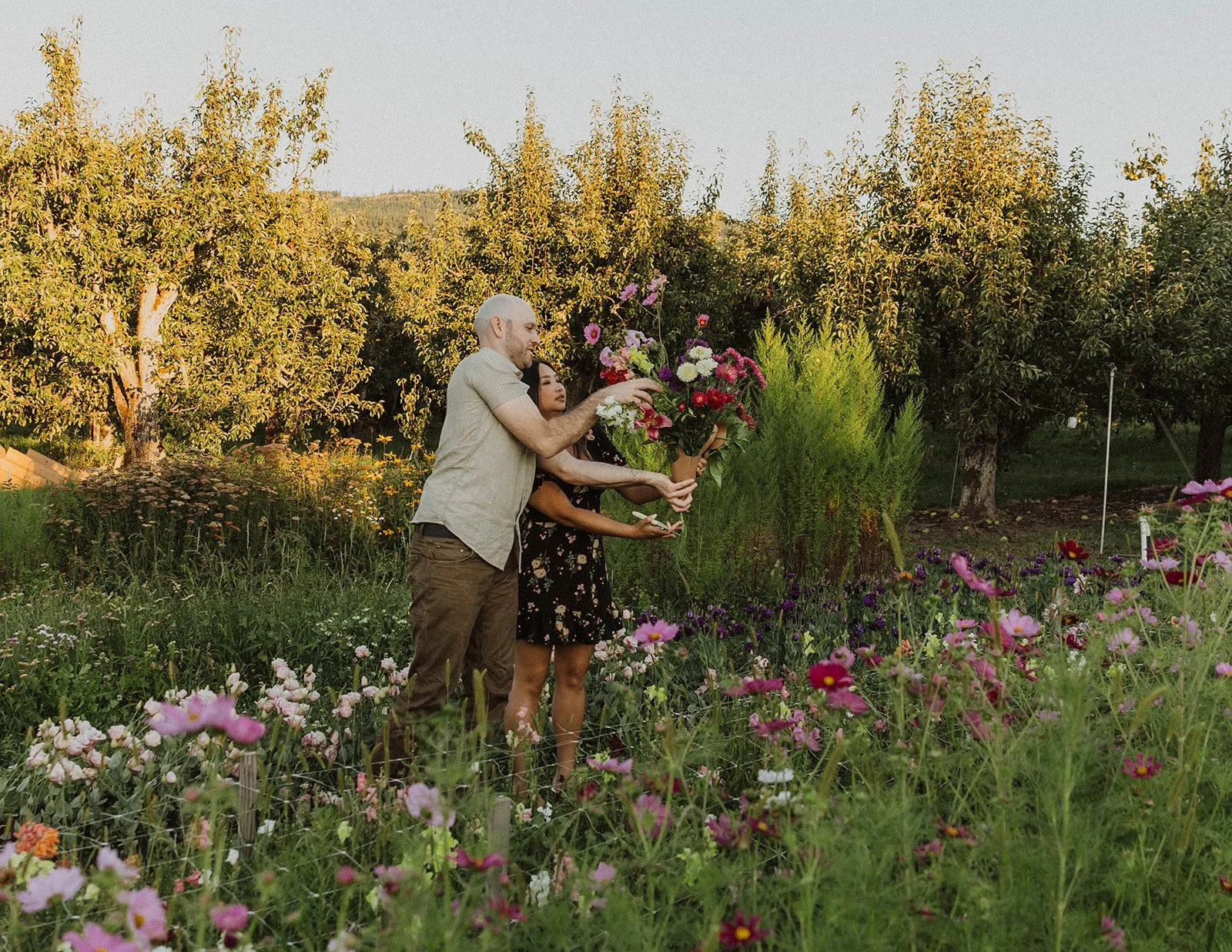 Engaged couple arranging a colorful bouquet together in a flower field during a flower farm engagement session.