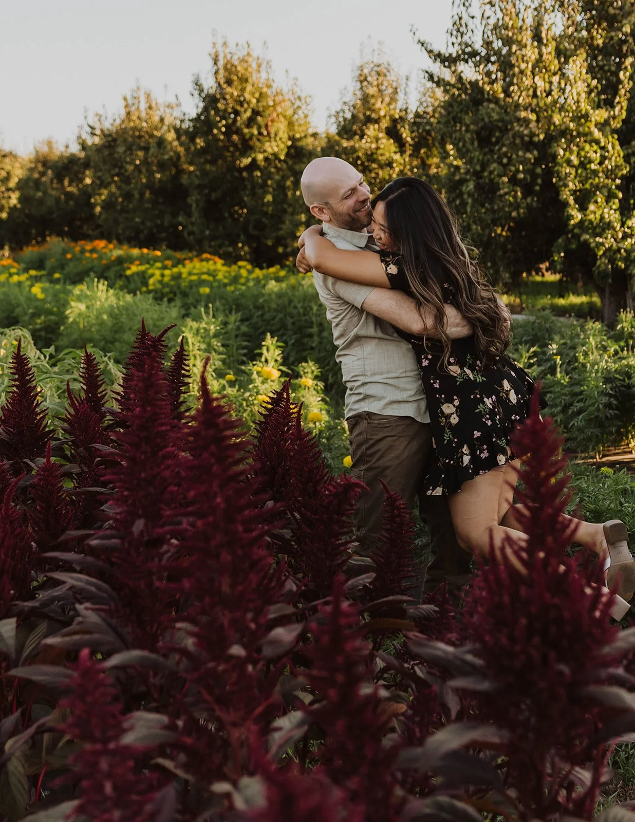 Couple sharing a joyful embrace among colorful flowers during a playful engagement session at a flower farm.