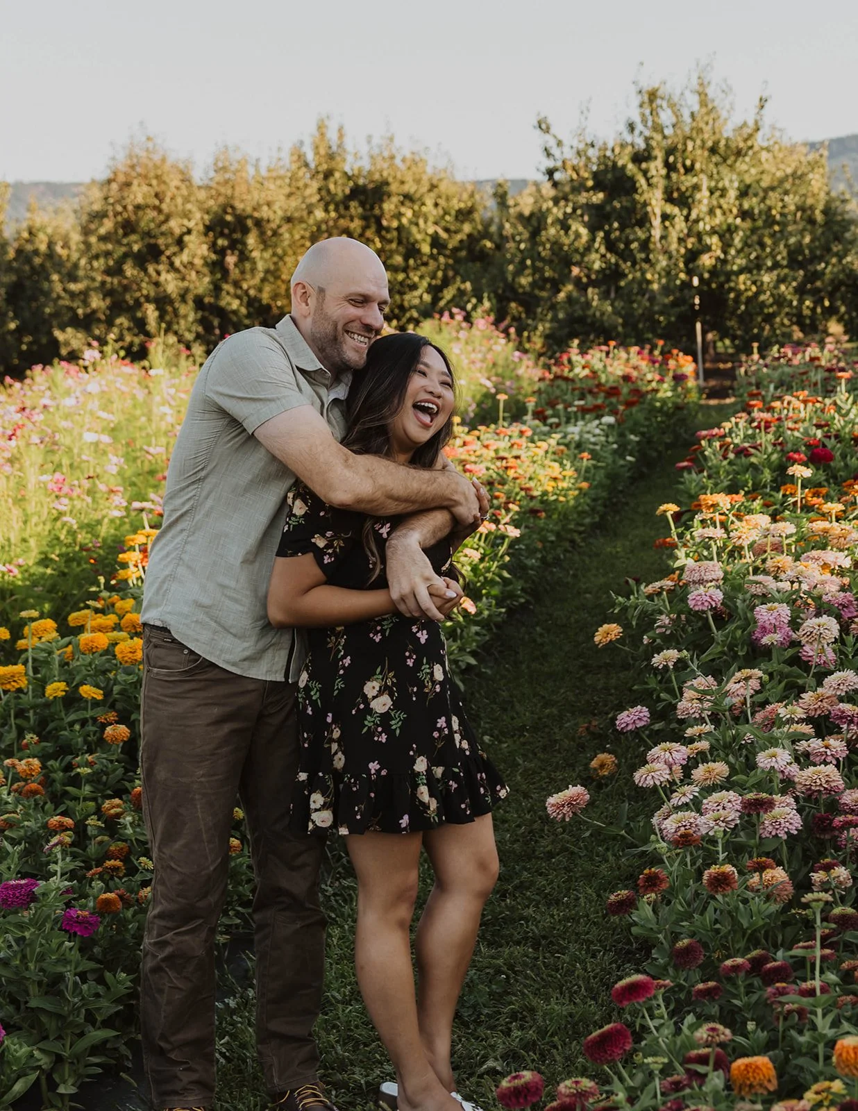 Couple laughing together while embracing in a colorful flower field during their engagement session.